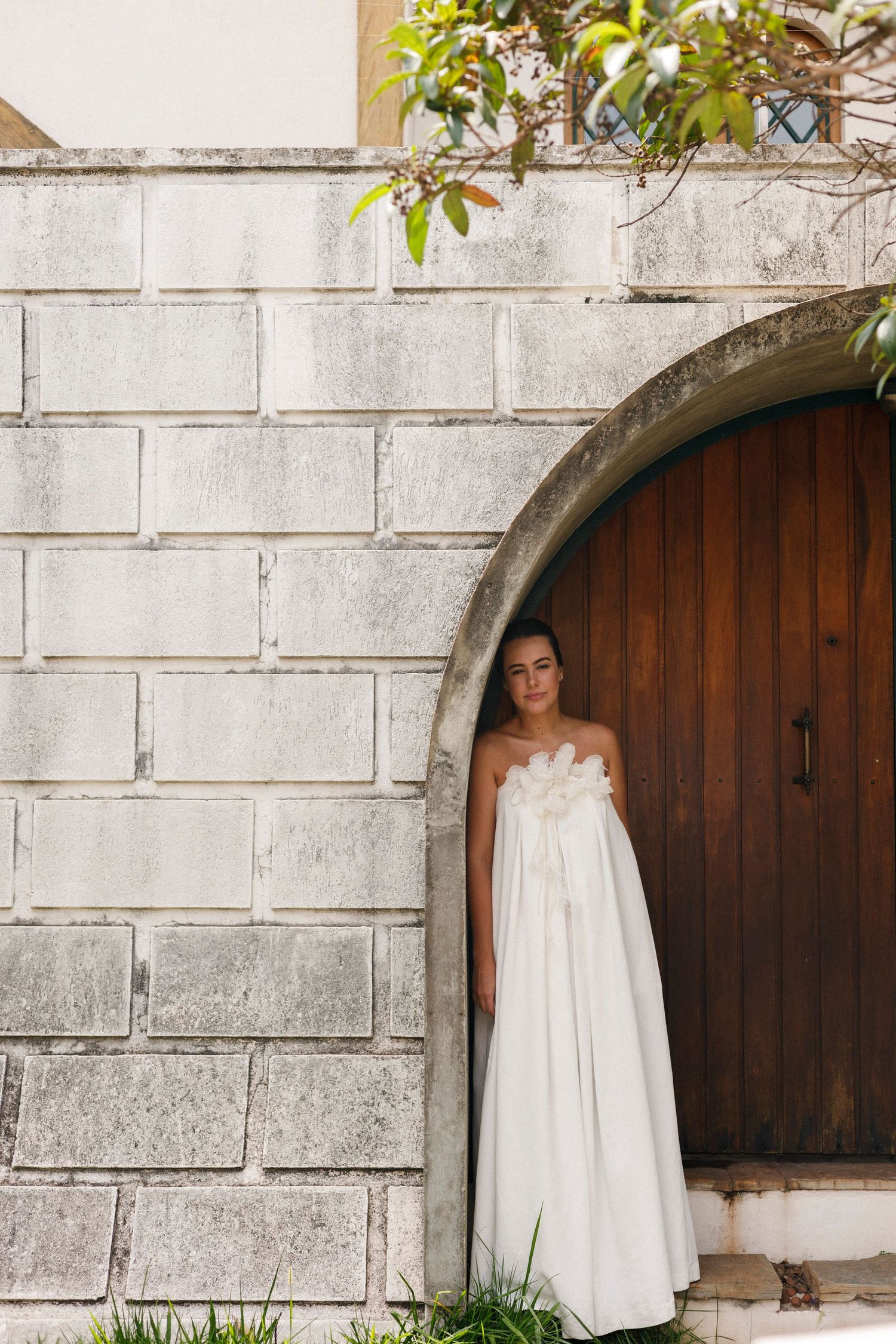 White wedding dress hanging in stone archway with wooden door.