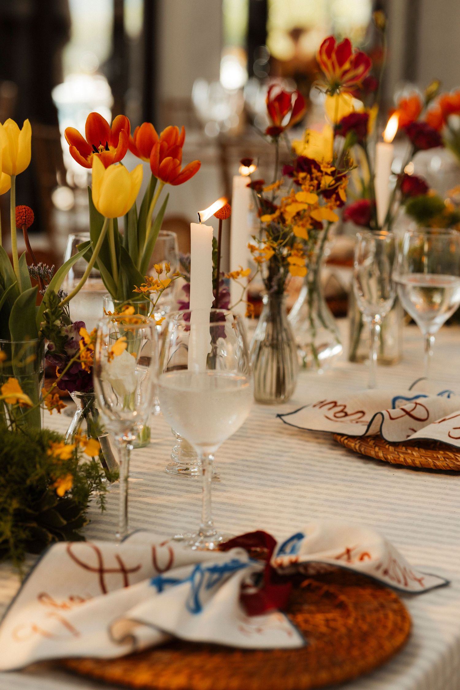 Elegant wedding table setting with colorful tulips, candles, and wine glasses on a white tablecloth.