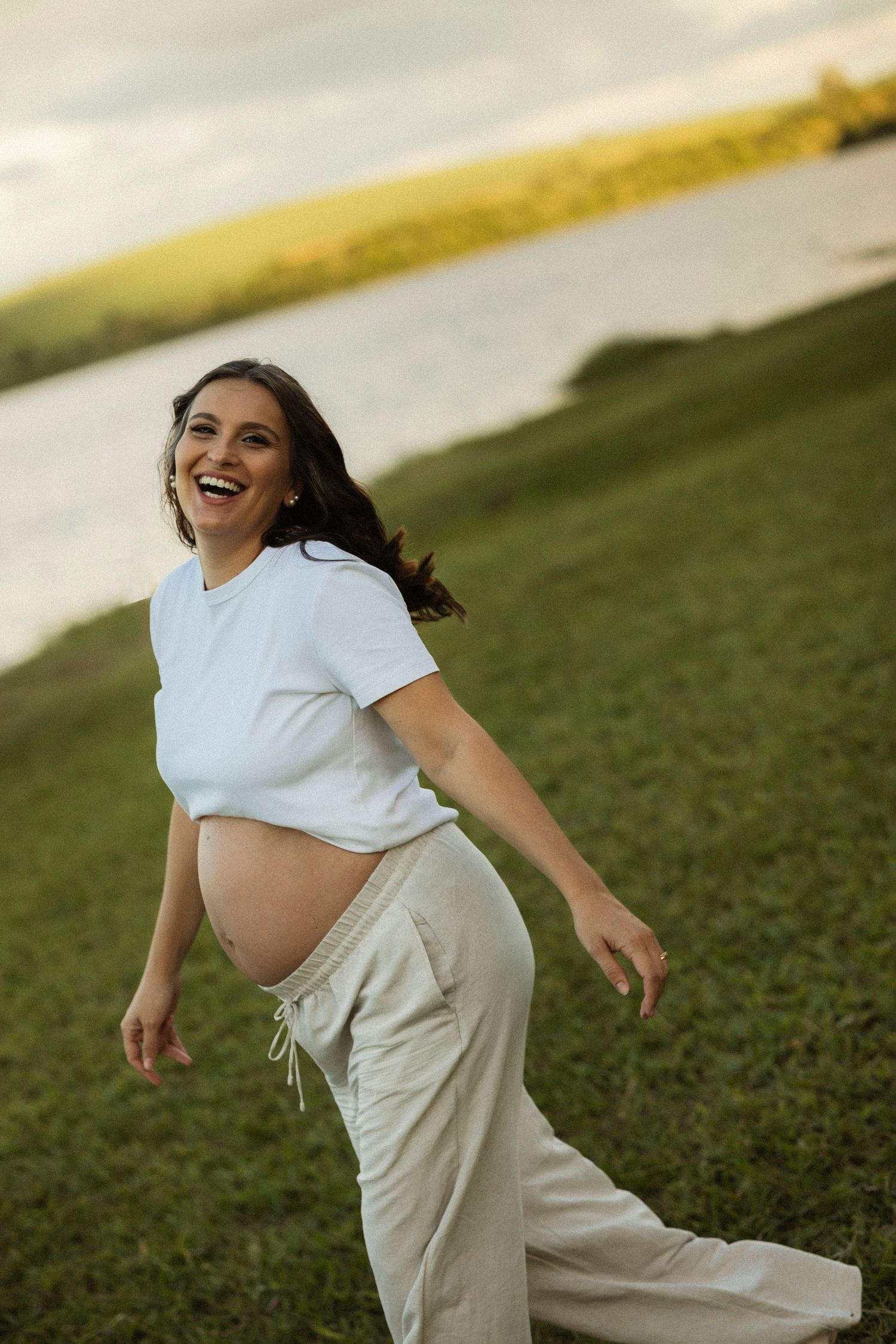 A person in a white shirt and beige pants dances joyfully outdoors against a sunset sky.