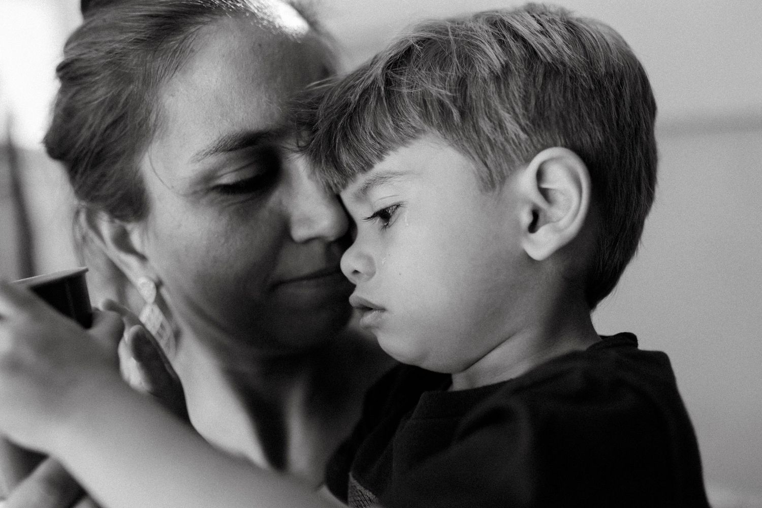 Black and white photo of a mother tenderly holding her young son close, sharing a quiet emotional moment.