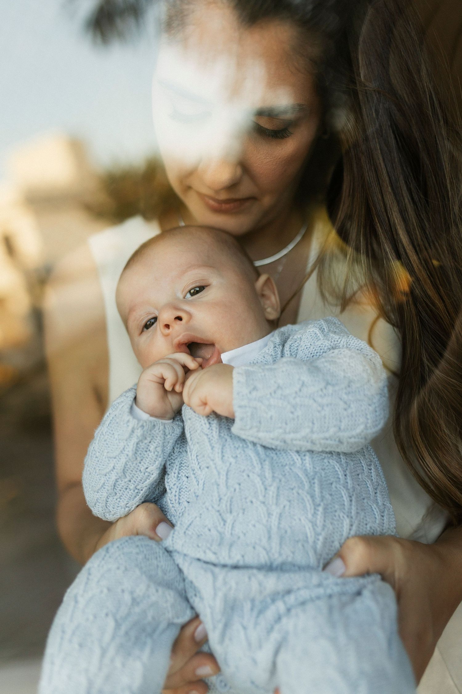A mother tenderly holds her newborn baby dressed in a blue knit outfit, sharing a peaceful moment together.