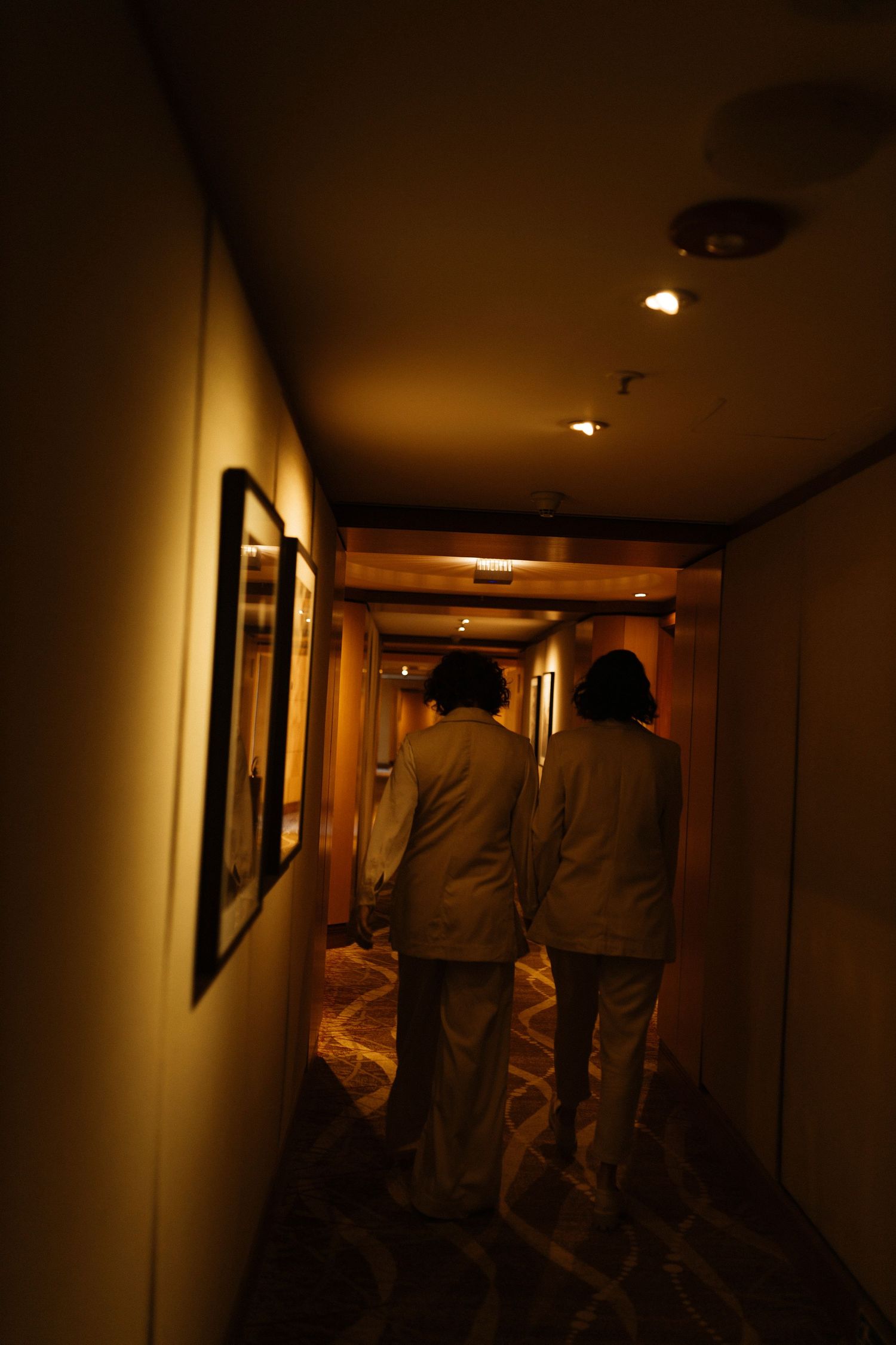 Dimly lit hallway with figures walking away from camera in warm ambient lighting.