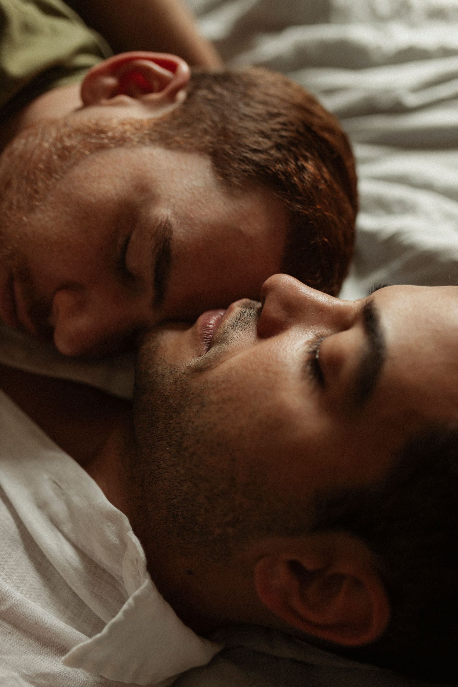 Close-up profile shot of someone resting on white bedding in moody lighting.