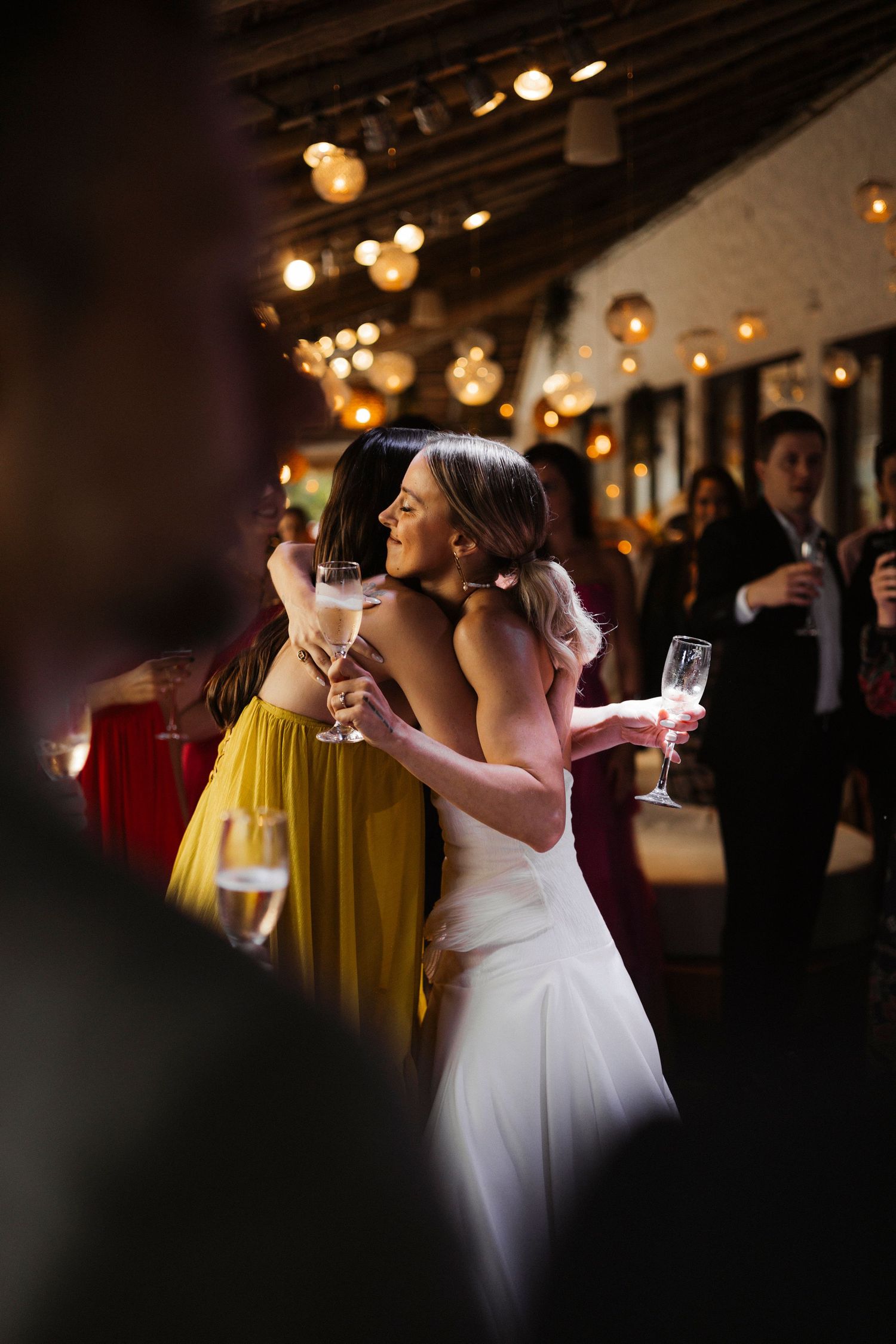 Wedding reception guests raise glasses for a toast under warm lighting.