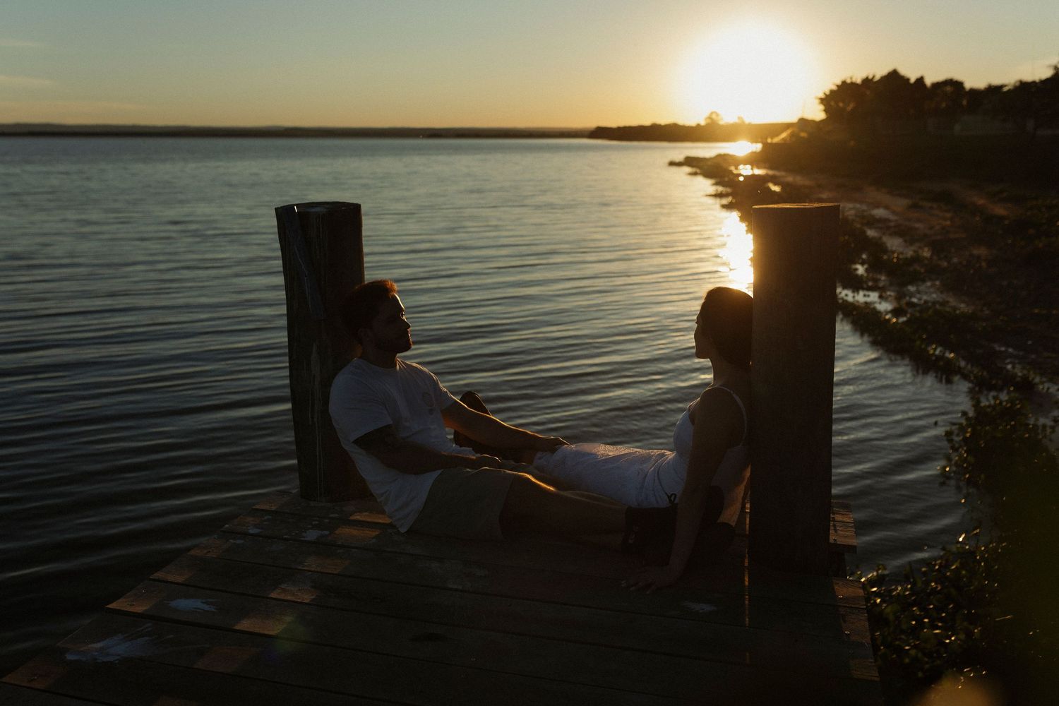 Sunset silhouettes by a waterfront dock with golden light reflecting on the water.