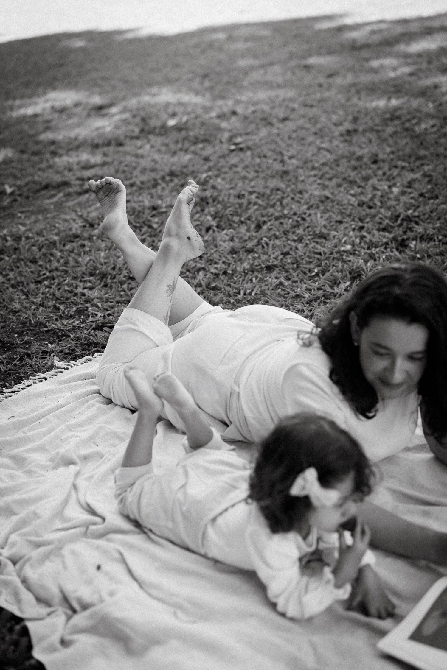 Black and white photo of a mother and young child lying on a blanket outdoors, smiling and playing together.