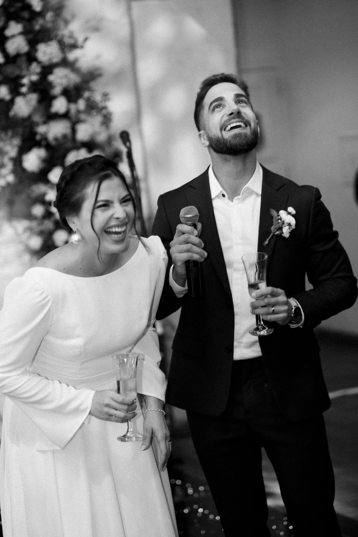 Wedding couple sharing champagne and laughing together during reception festivities.