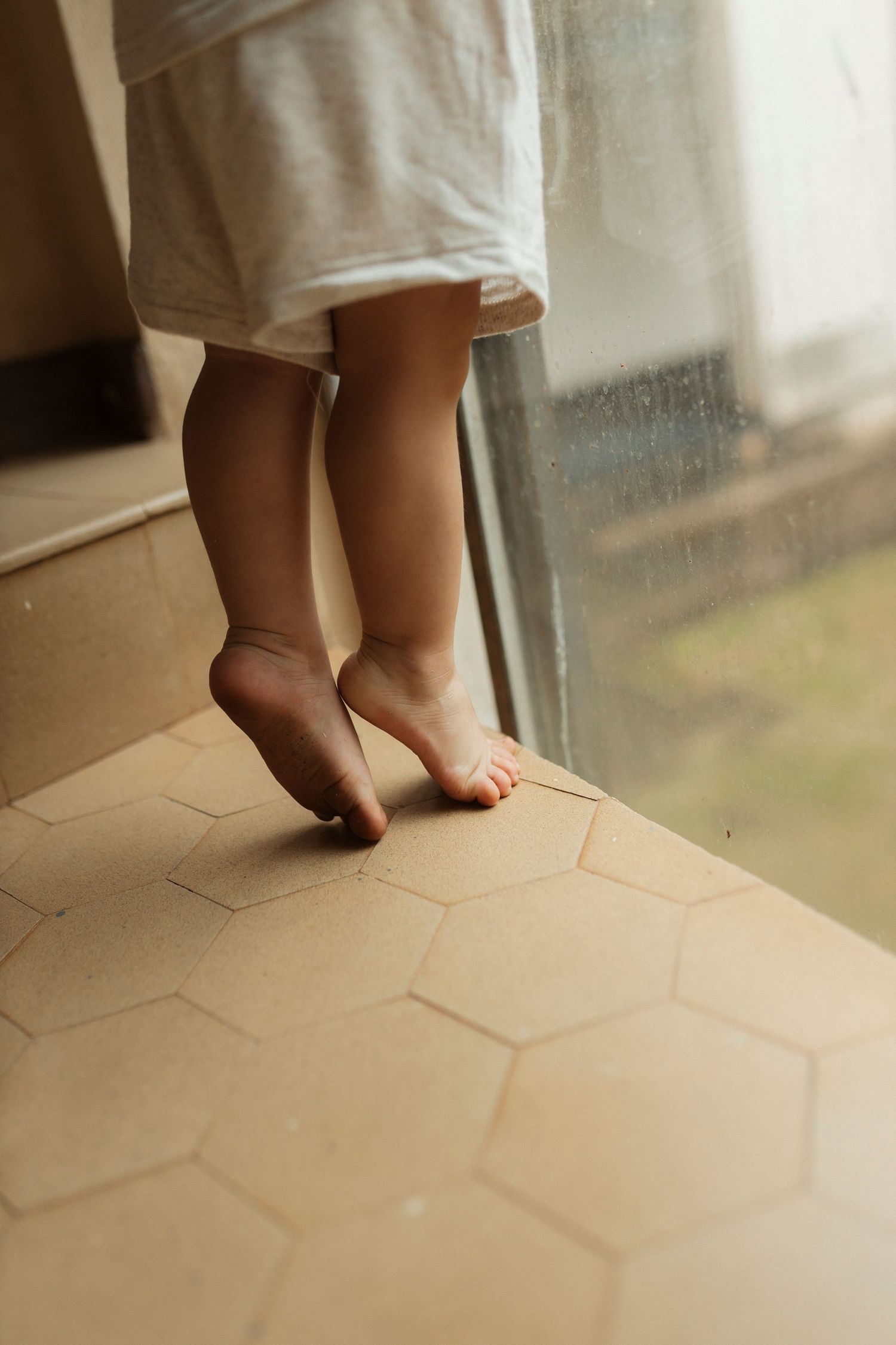 Close-up shots of small bare feet walking on hexagonal floor tiles.