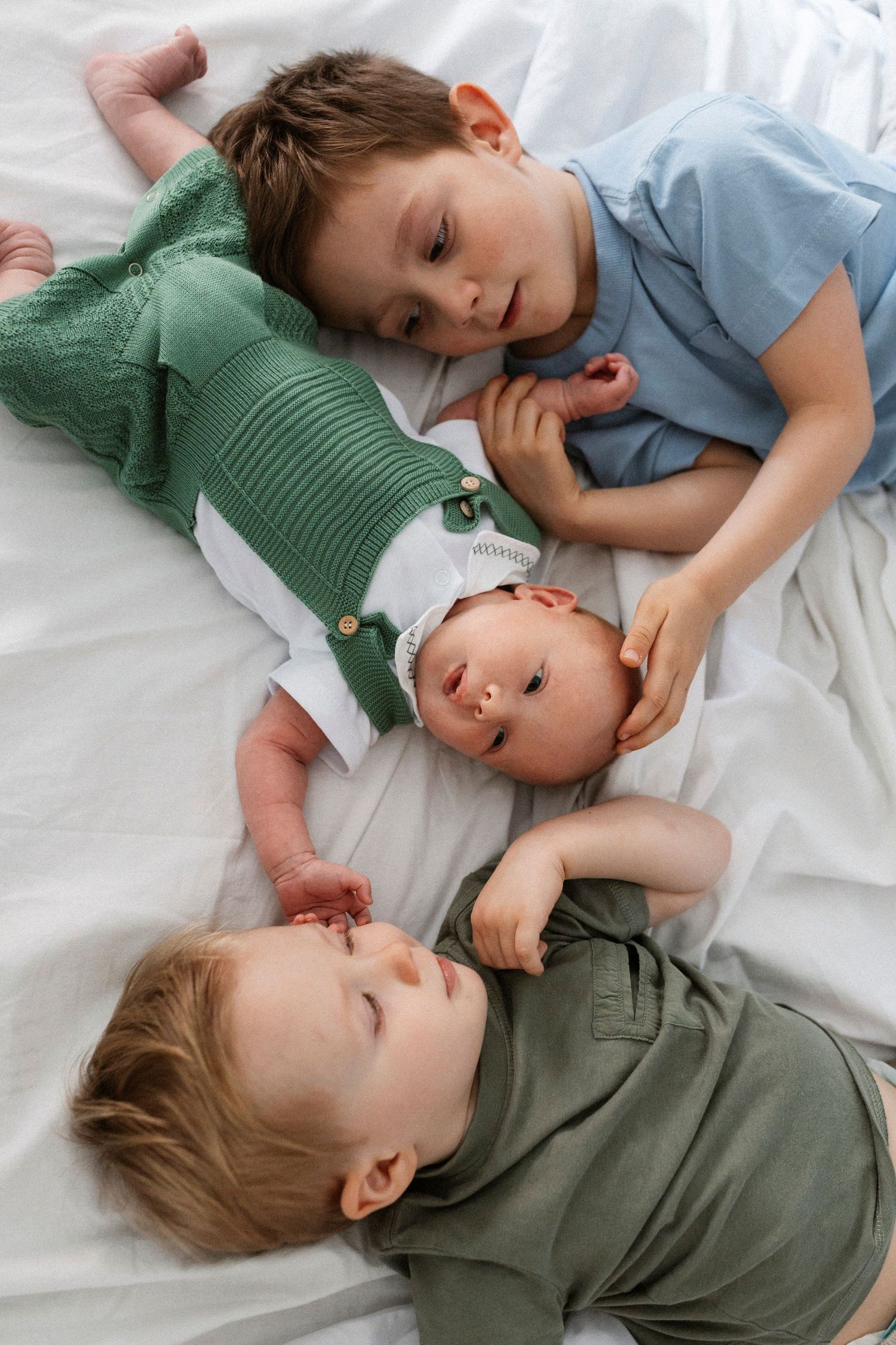Two children in casual clothing rest peacefully on white bedding.
