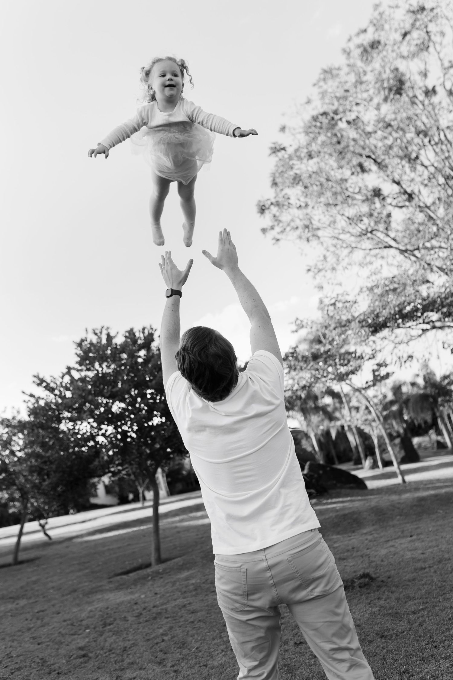 Black and white photo of playful moments in a park with a child being lifted in the air.
