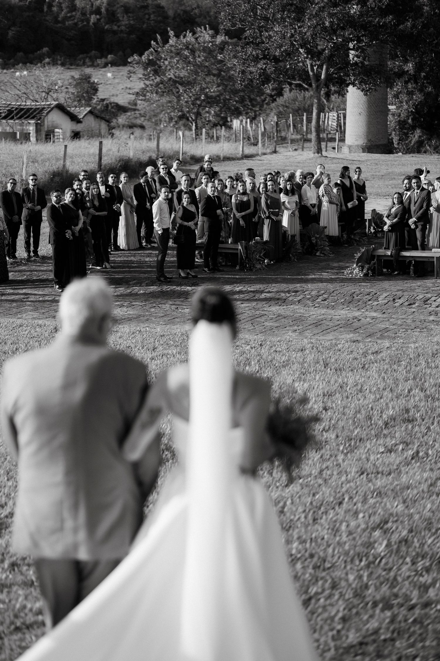 Bride and groom walking towards wedding guests gathered outdoors in black and white photograph.