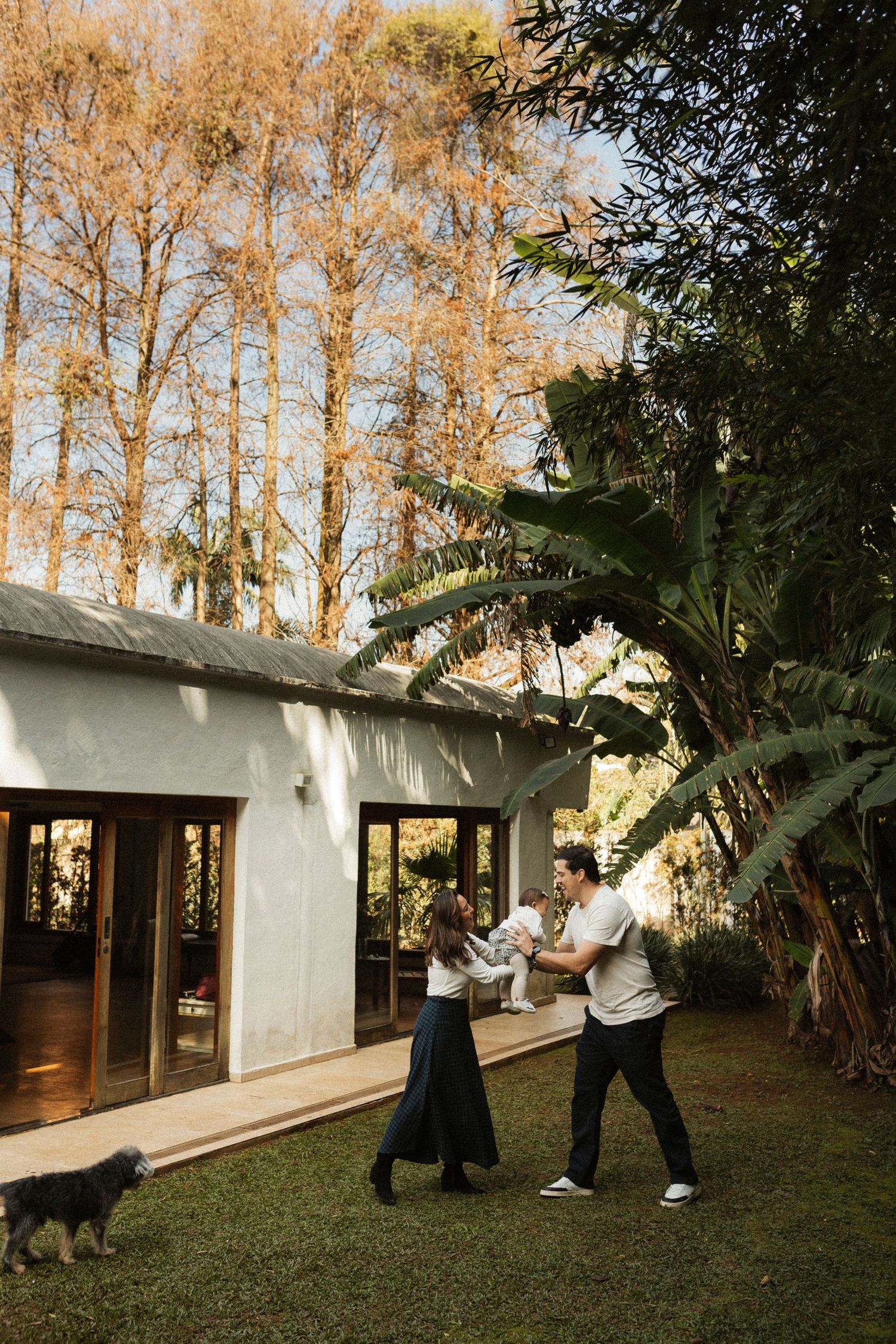A couple dances in a lush backyard garden beside a modern home, surrounded by tropical plants and autumn trees.