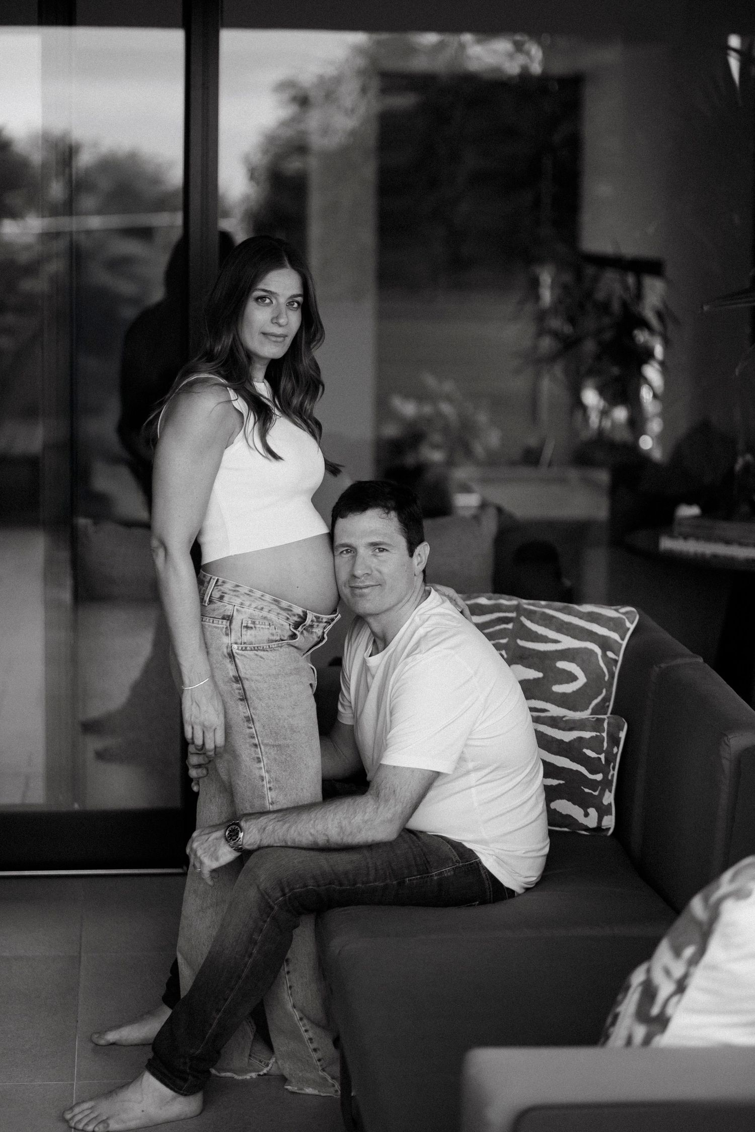 Casual couple lounging on a dark leather couch in black and white photography.