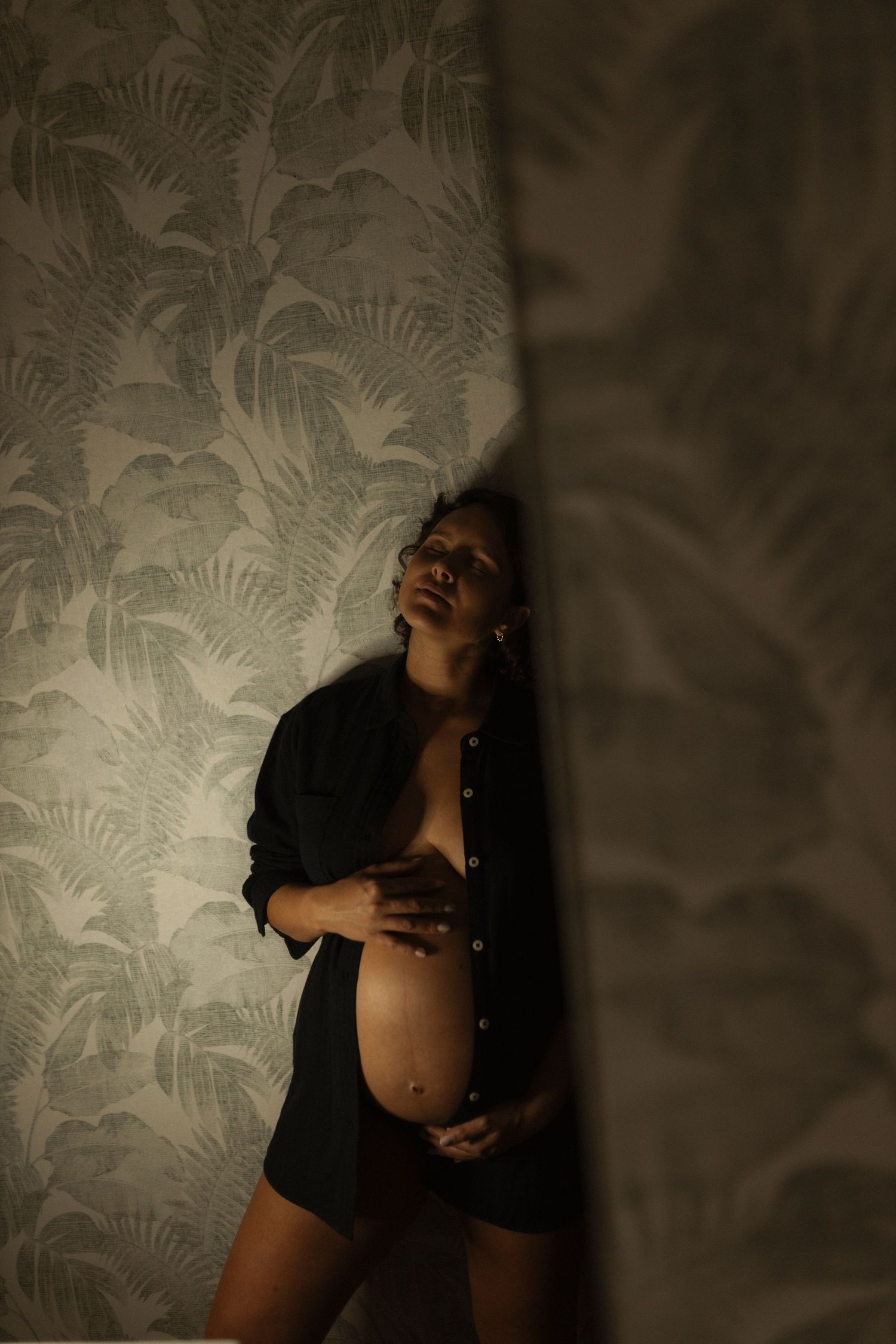 Artistic boudoir photoshoot featuring dramatic lighting and textured wallpaper backdrop.
