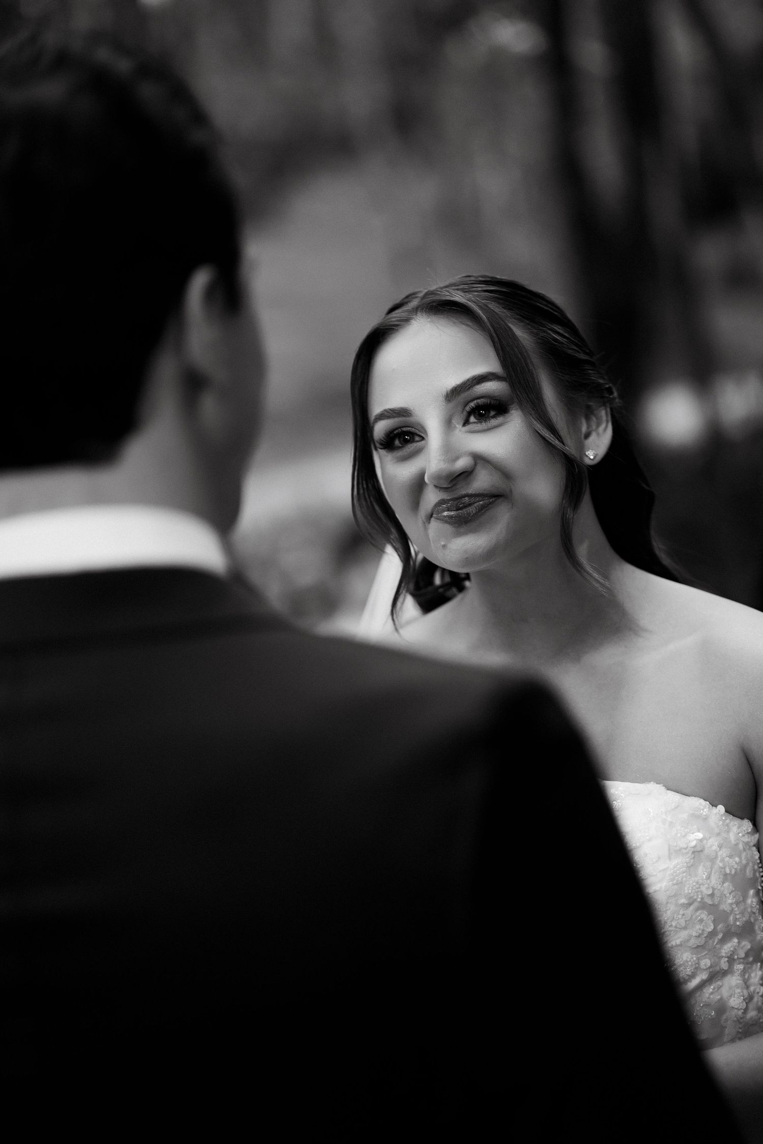 Black and white wedding photo of a smiling bride in a lace dress looking lovingly at the groom.