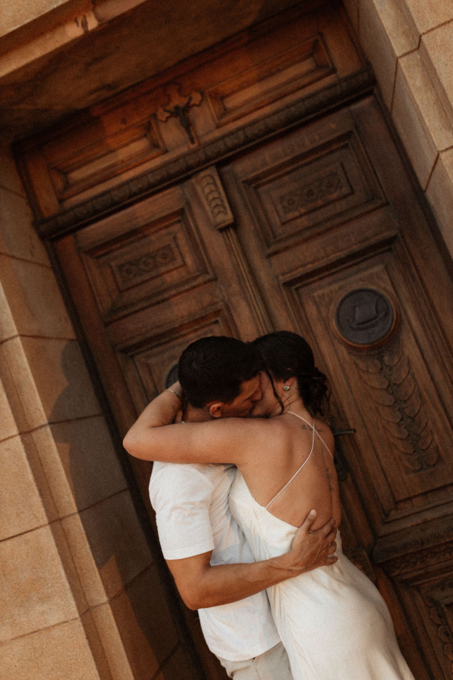 Romantic couple embraces against ornate wooden doors in an intimate moment.