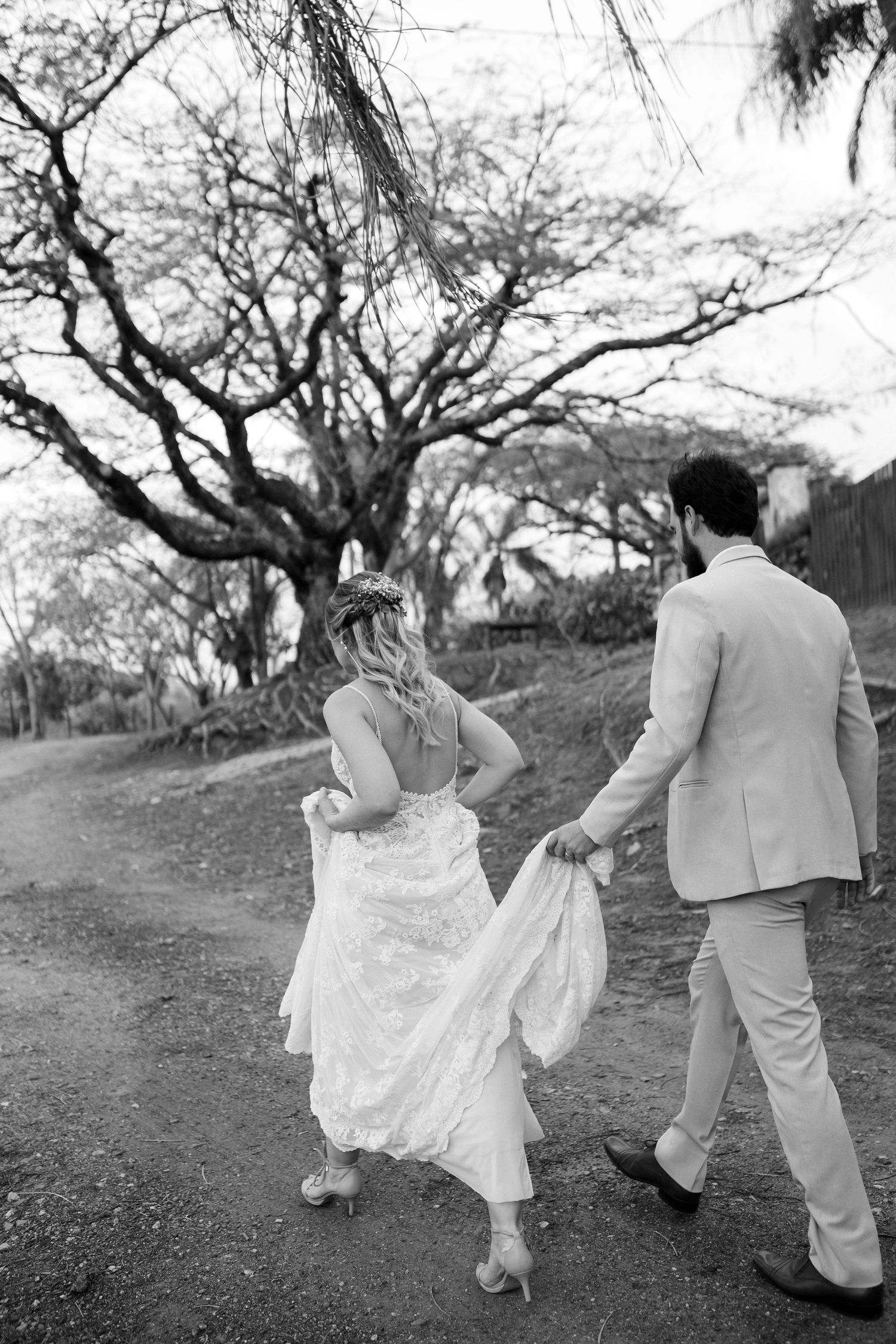 Playful black and white sequence of newlyweds running together on a tree-lined path.