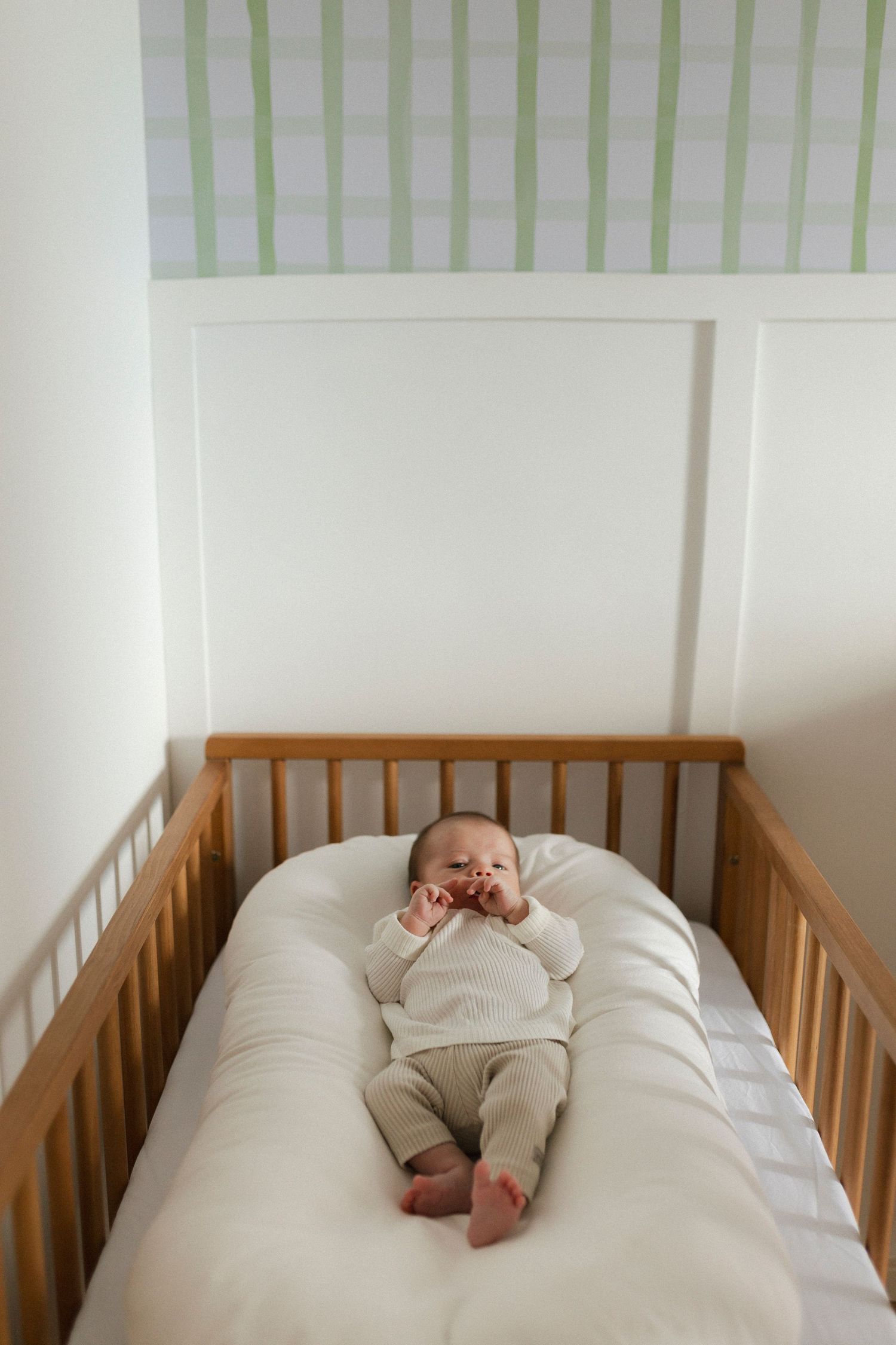 Series of photos showing a baby lying in a wooden crib with striped wallpaper.