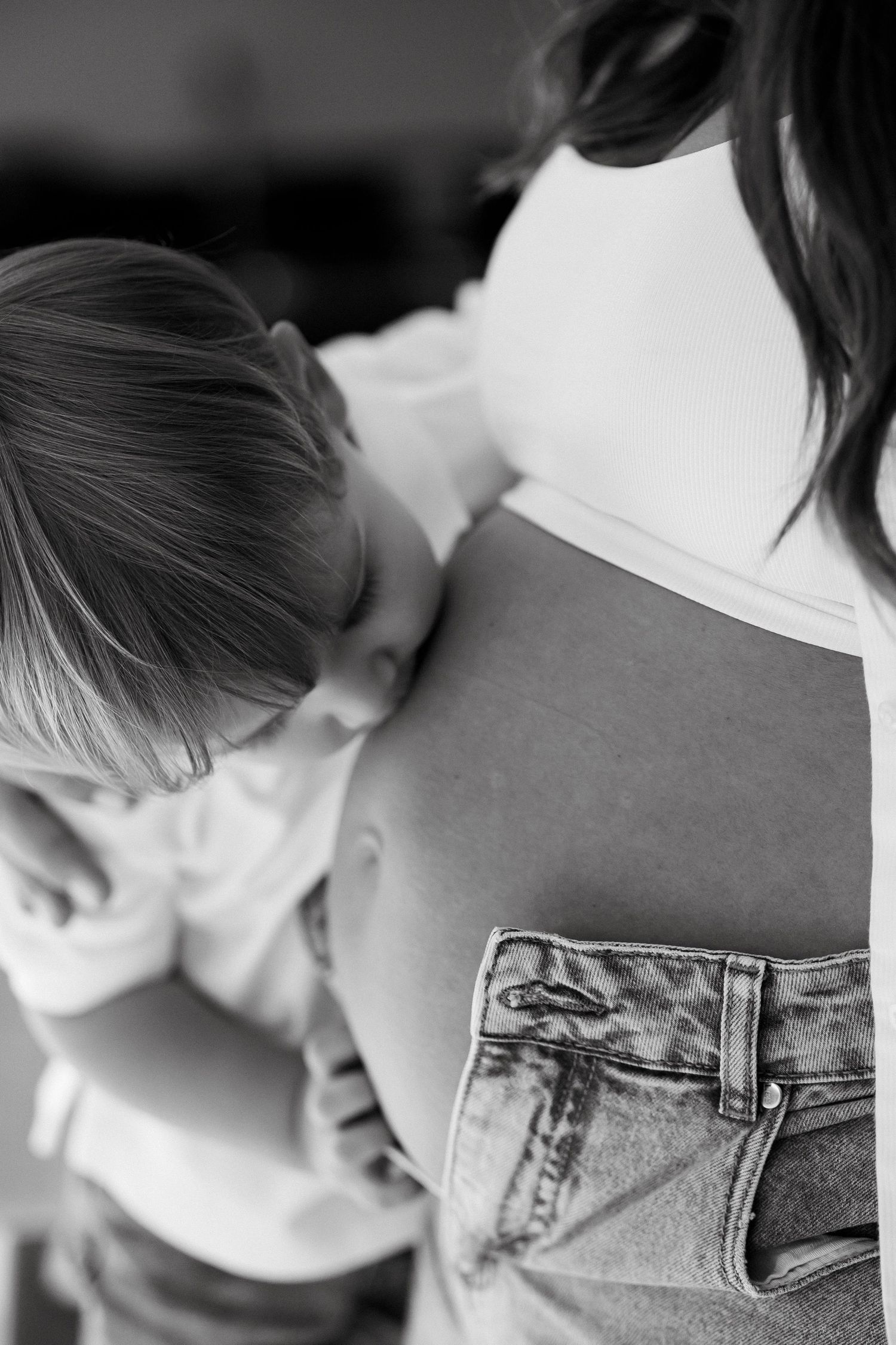 A tender black and white photograph showing a child resting against someone wearing denim jeans and a white top.
