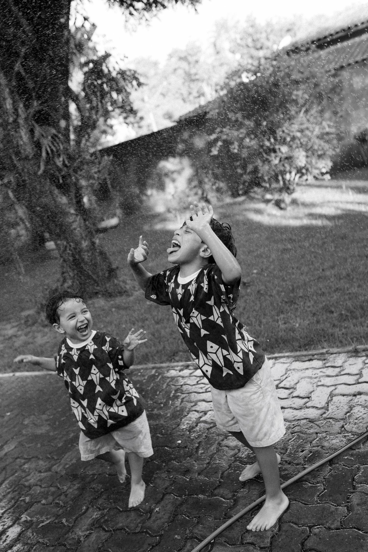 A sequence of black and white photos showing joyful children playing and laughing together on stone pavers outdoors.
