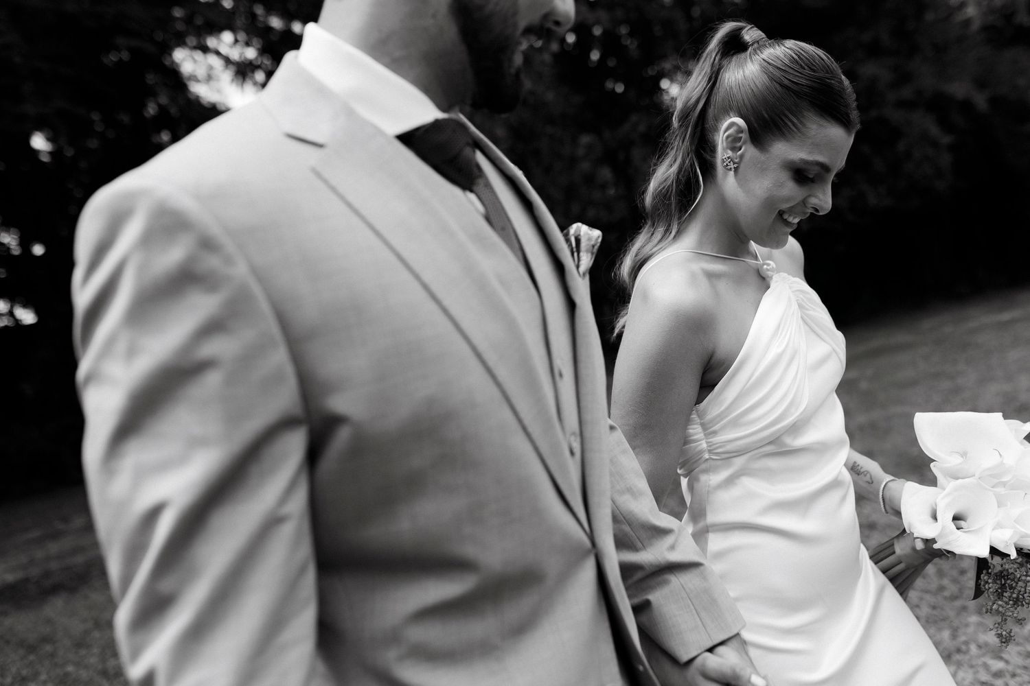 Black and white photo of a bride in a white halter dress and groom in a light gray suit walking outdoors.