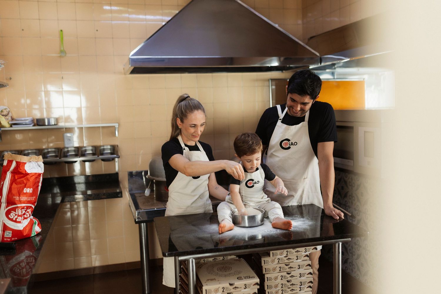 Family gathering in commercial kitchen space with cooking equipment visible.