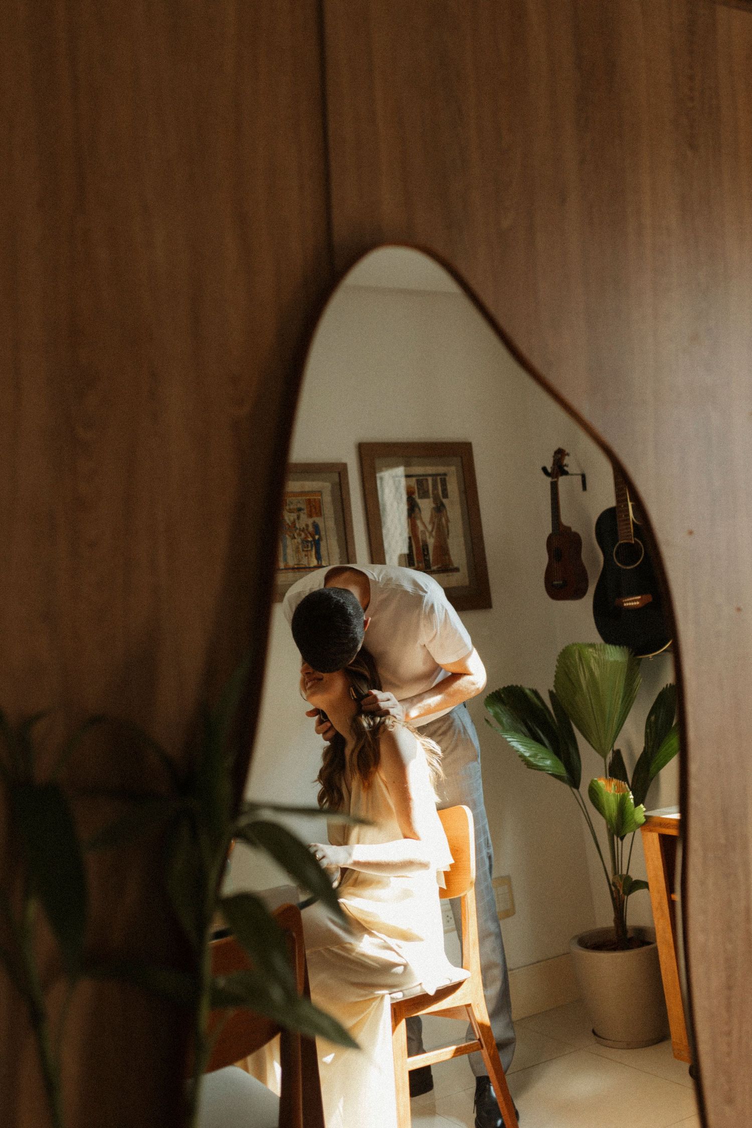 Couple in white clothing embracing in a warmly lit room with houseplants and decor.