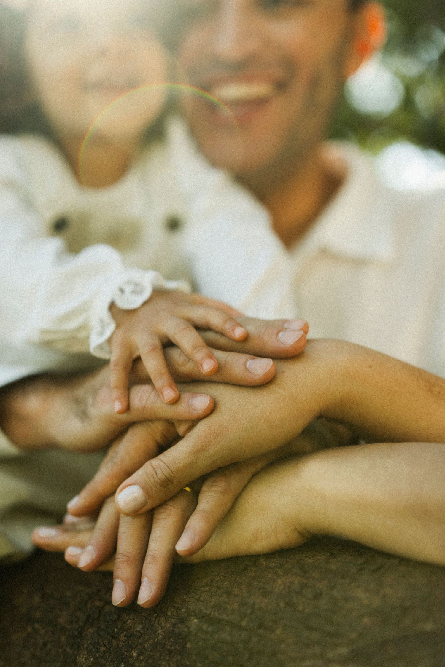 Family stacking hands together outdoors, smiling parents with child in warm sunlight, symbolizing love and unity.