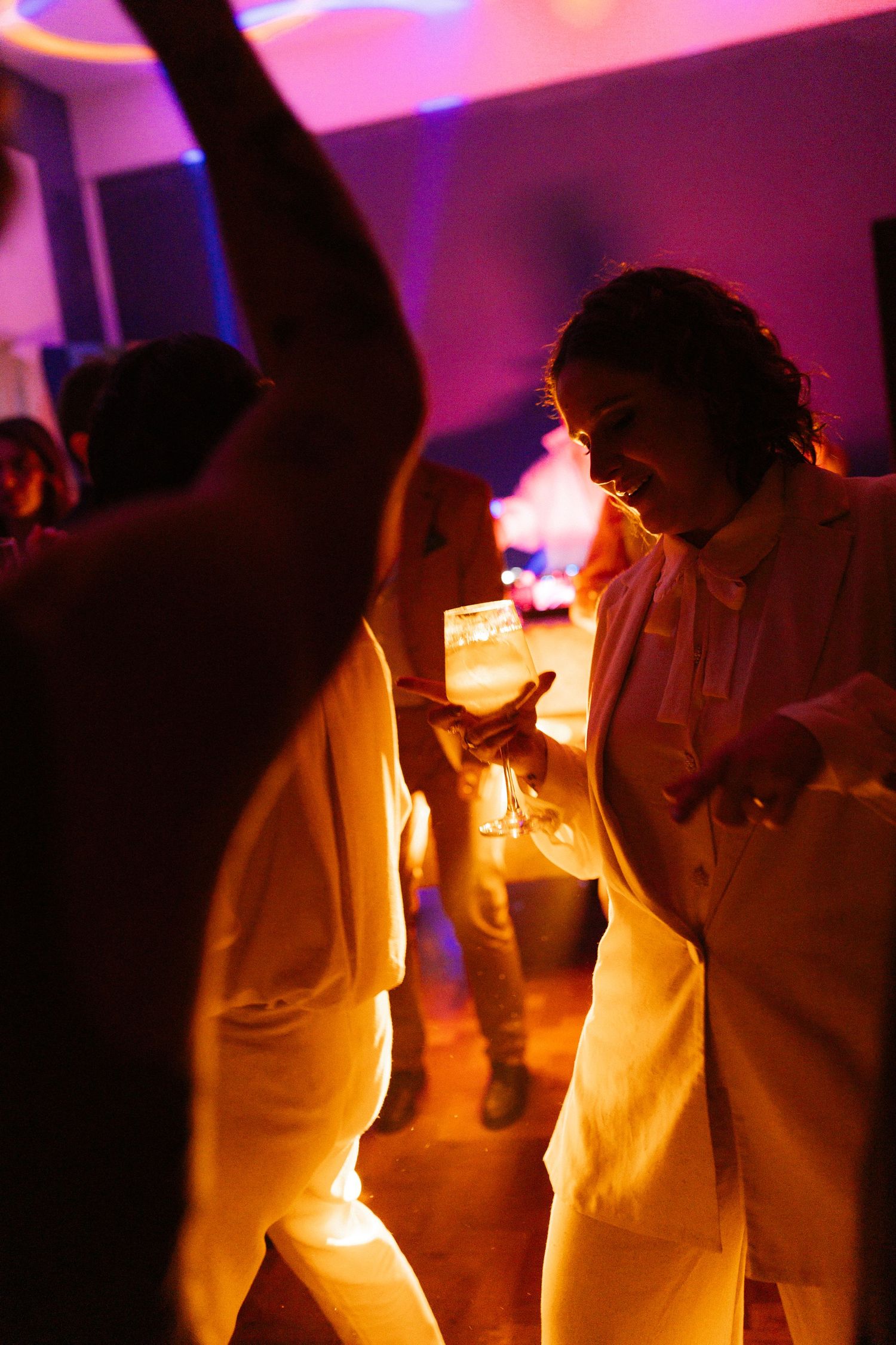 People dancing in white outfits under purple party lights creating a festive atmosphere.