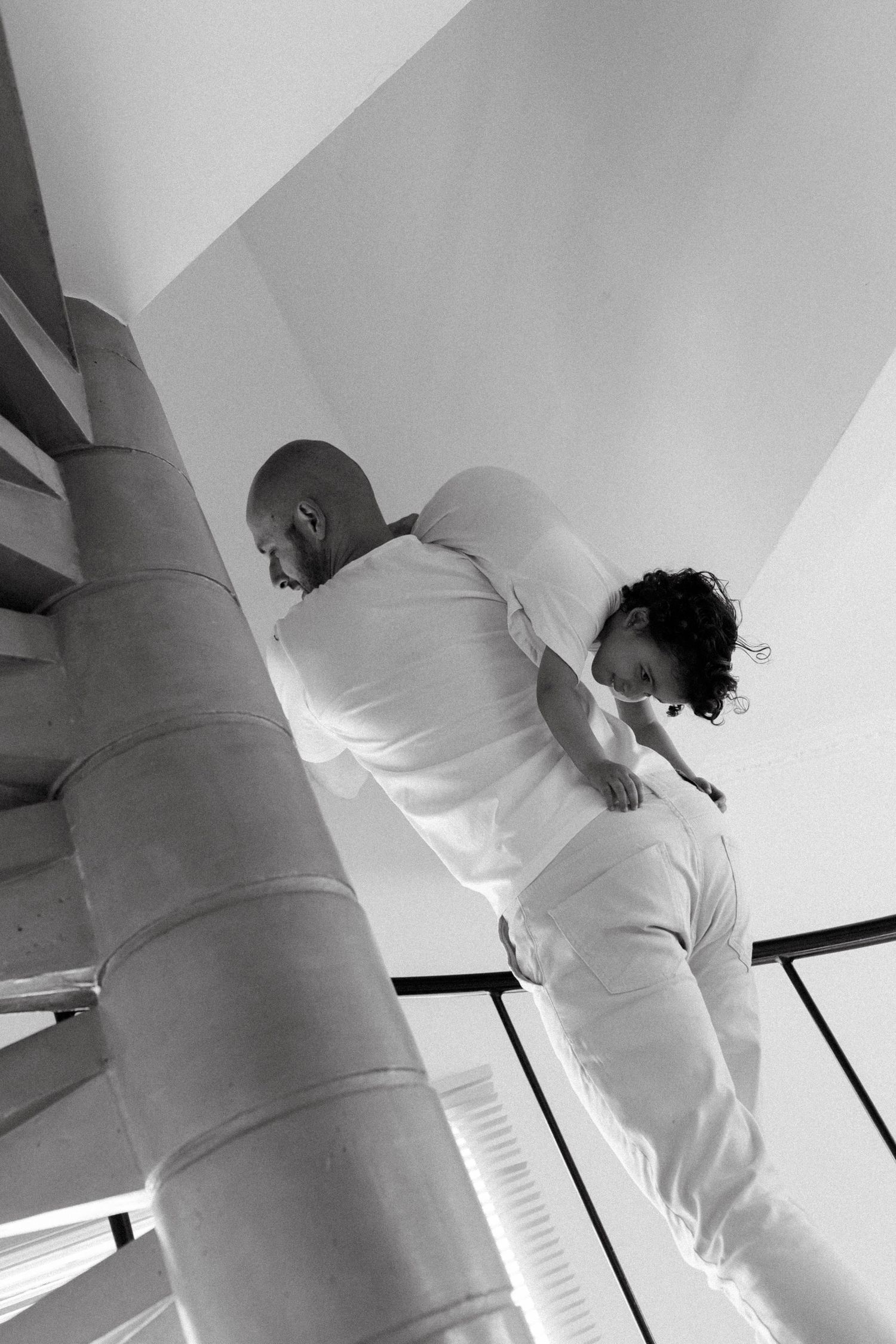 Black and white photo of two people in white clothing on a spiral staircase, viewed from below.