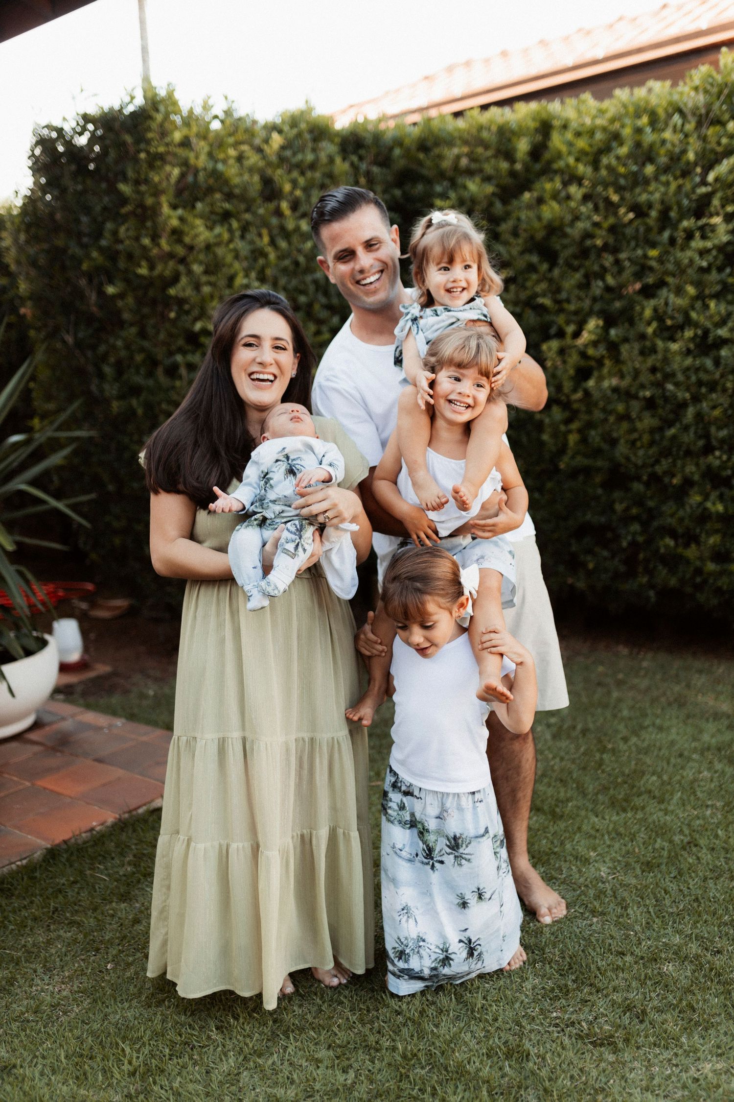 Family portrait of group in light summer dresses standing on grass in backyard.