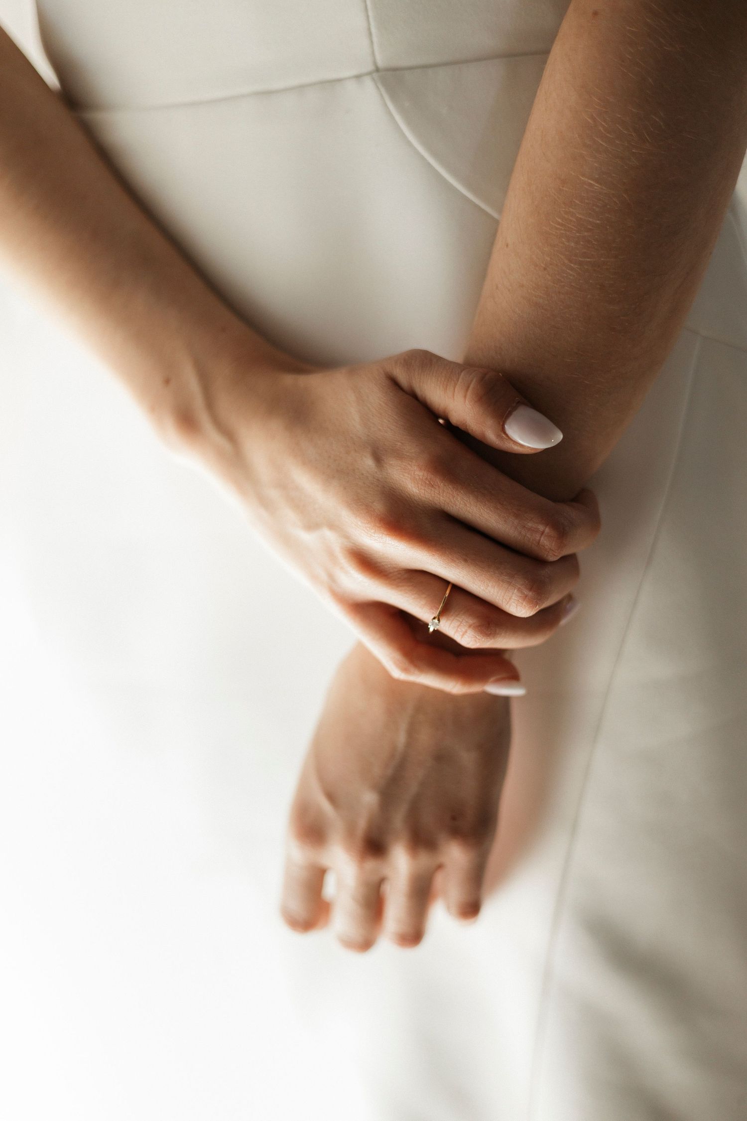 Close-up of hands resting on white fabric with soft natural lighting.