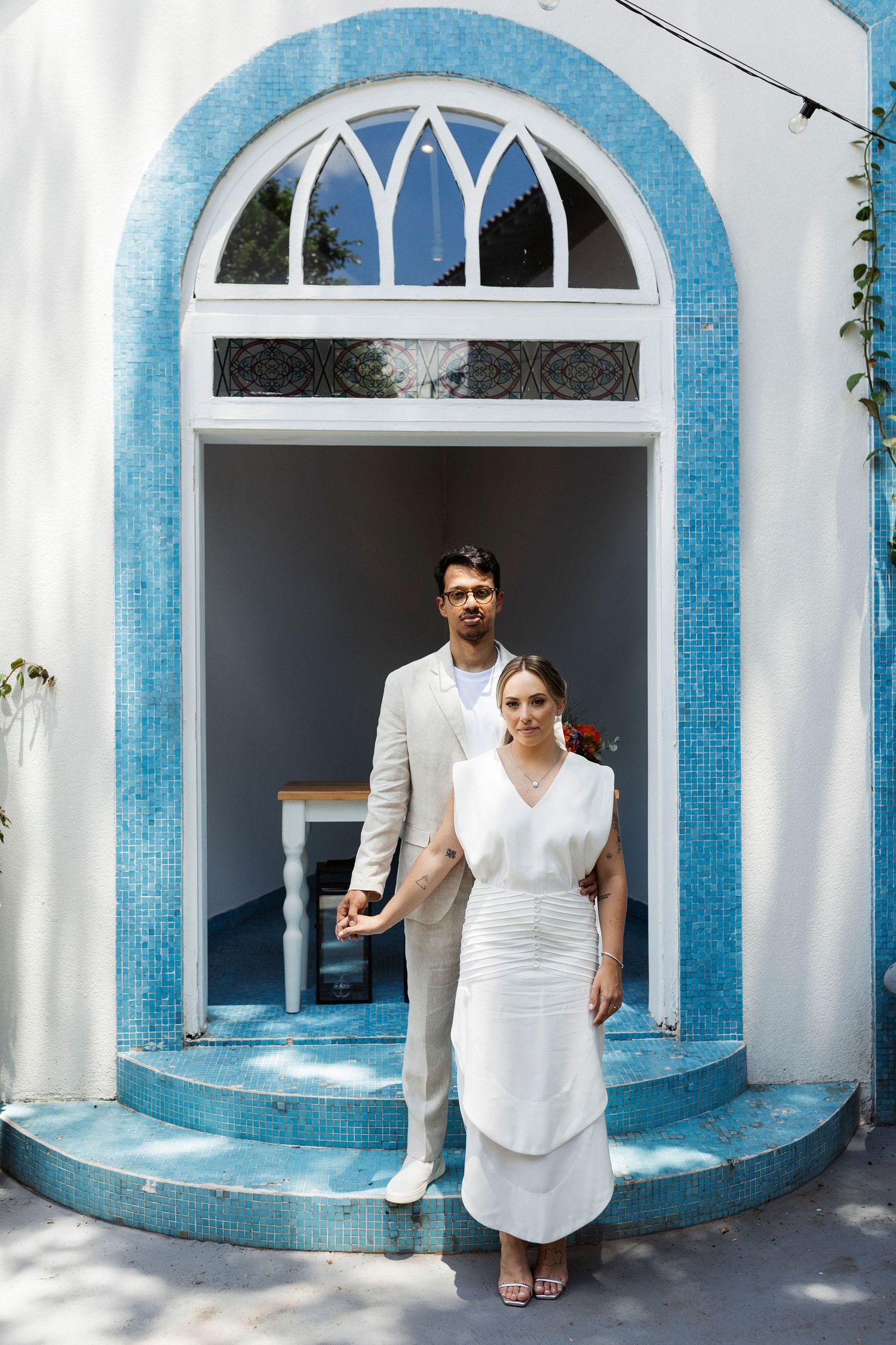 Wedding couple poses in ornate blue and white arched doorway entrance.