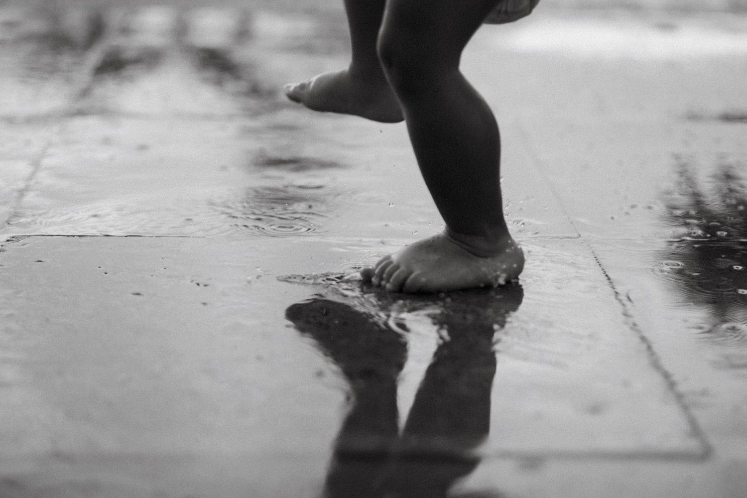 Close-up of feet splashing in puddles on a rainy day.