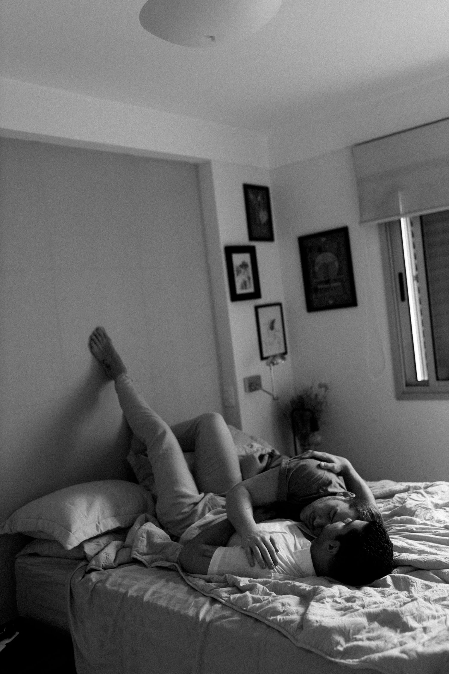 Figure lying on unmade bed in a room with framed artwork on walls.