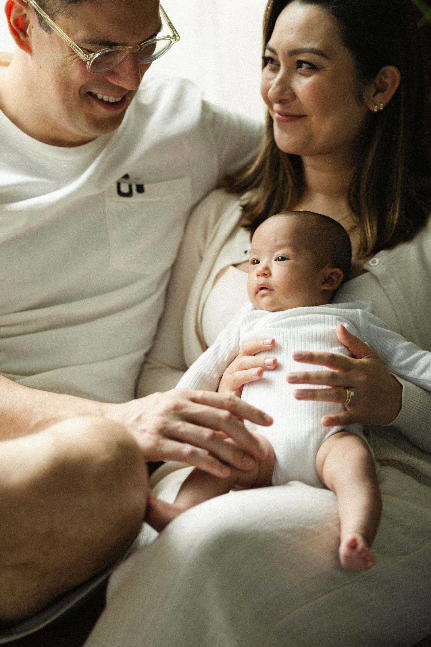 Intimate family moment with newborn baby in white onesie resting on soft couch.