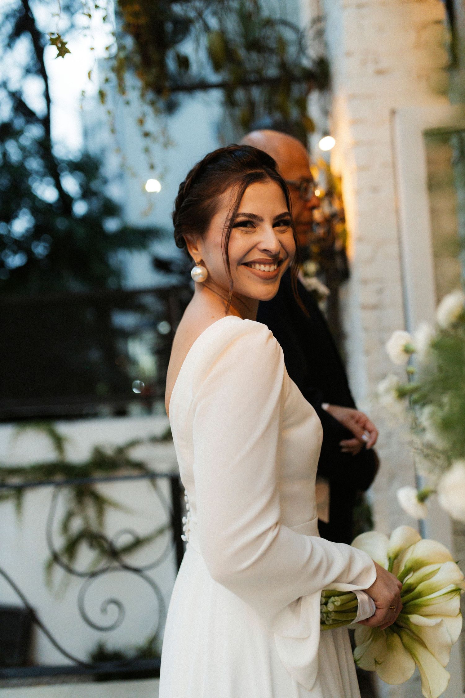 Outdoor wedding scene with white dress and calla lily bouquet against stone architecture.
