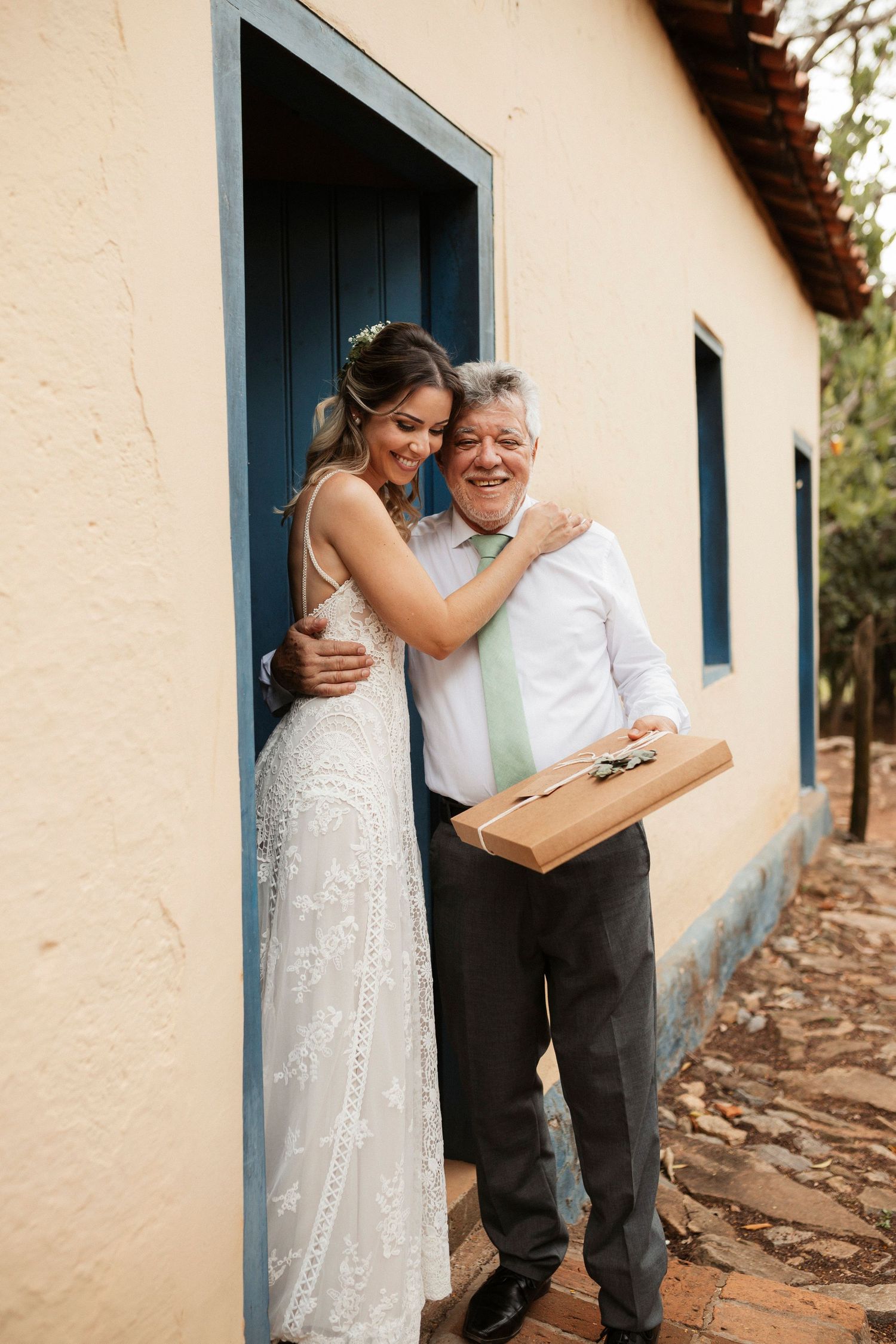 Emotional moment between a bride in white lace and an older man against a cream colored wall.