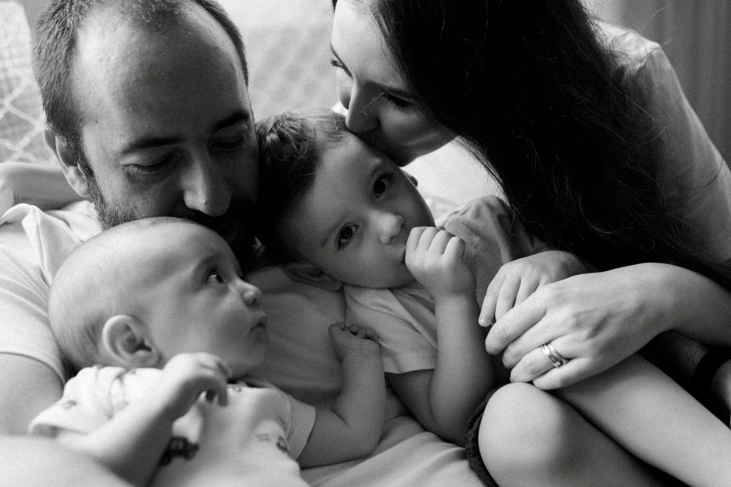 Black and white photo of parents lovingly cuddling two babies in an intimate family portrait.