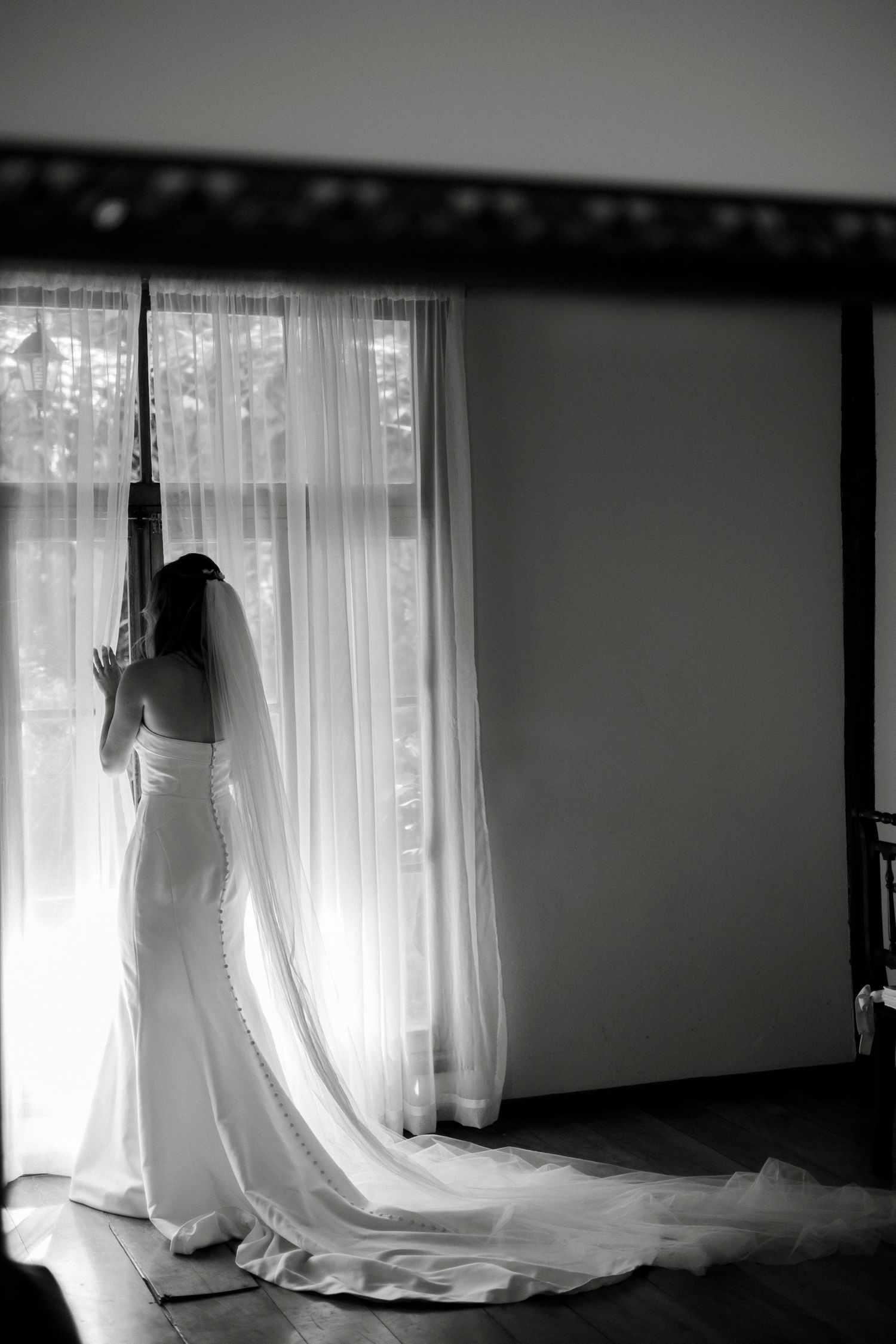 Silhouette of wedding dress against backlit window creating dramatic shadows.