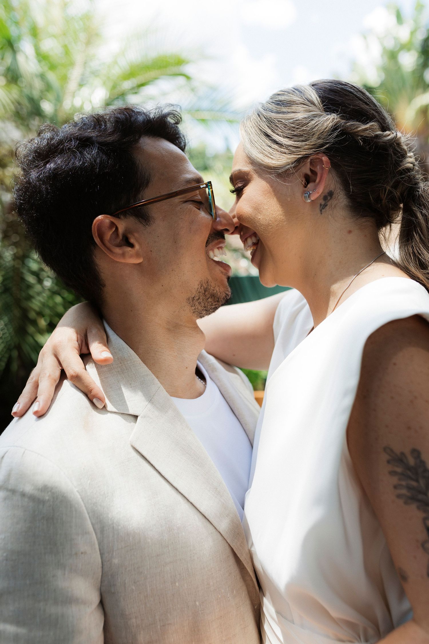 Intimate wedding couple in white attire sharing tender kisses against a garden backdrop.