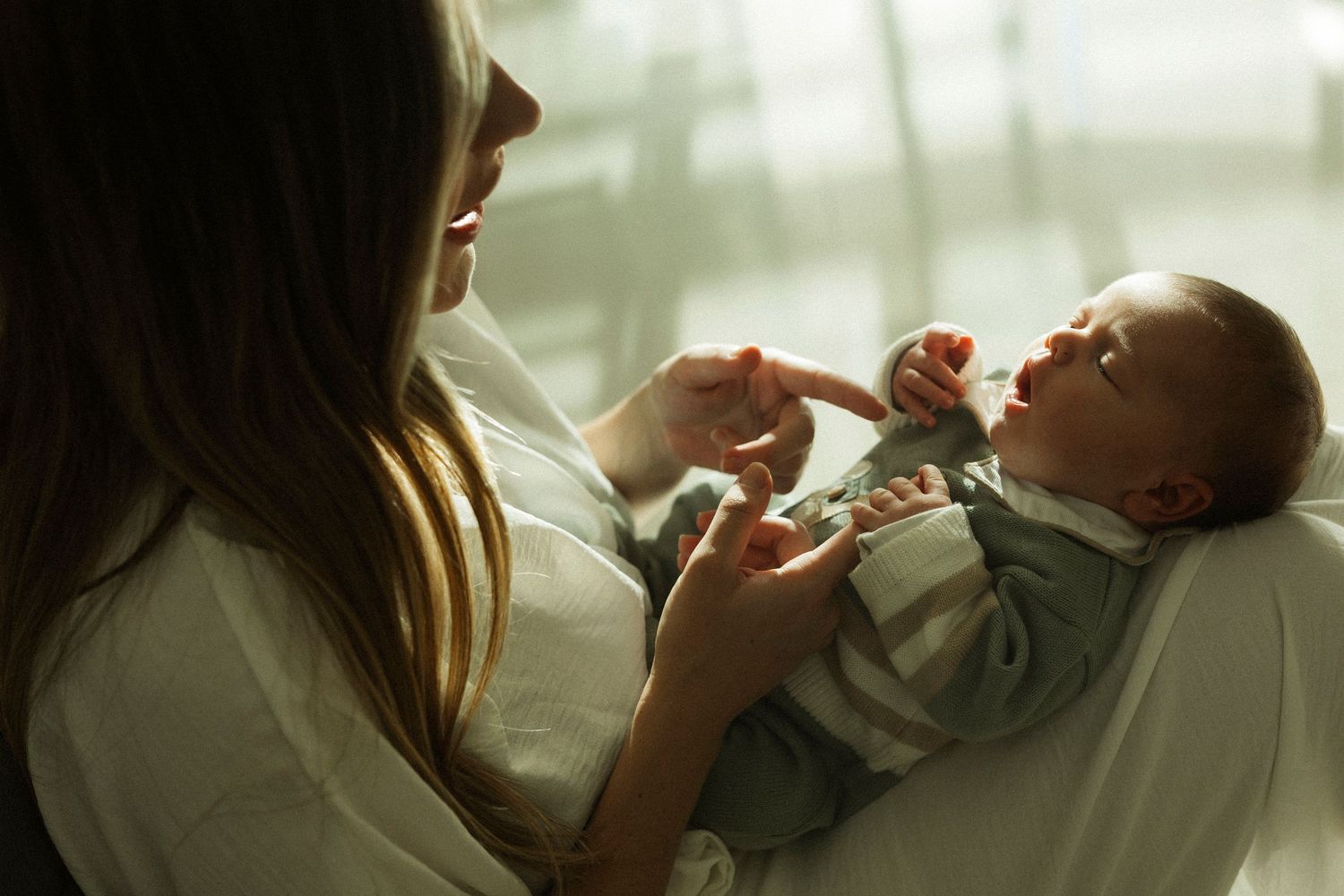 Mother tenderly holding and interacting with her newborn baby by a bright window.