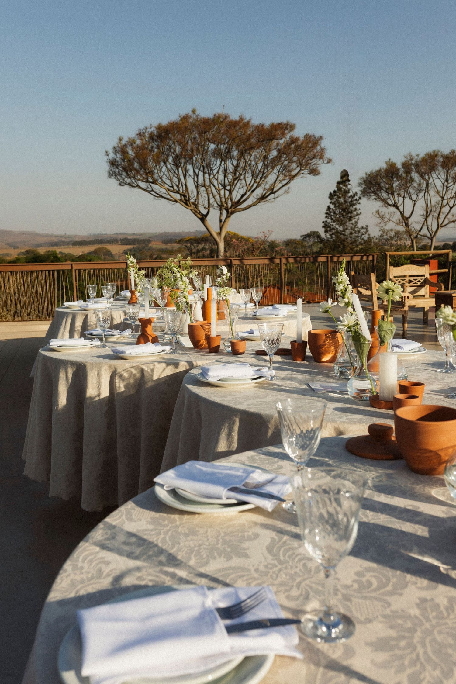 Elegant outdoor reception tables set with white linens and potted plants against a scenic backdrop.