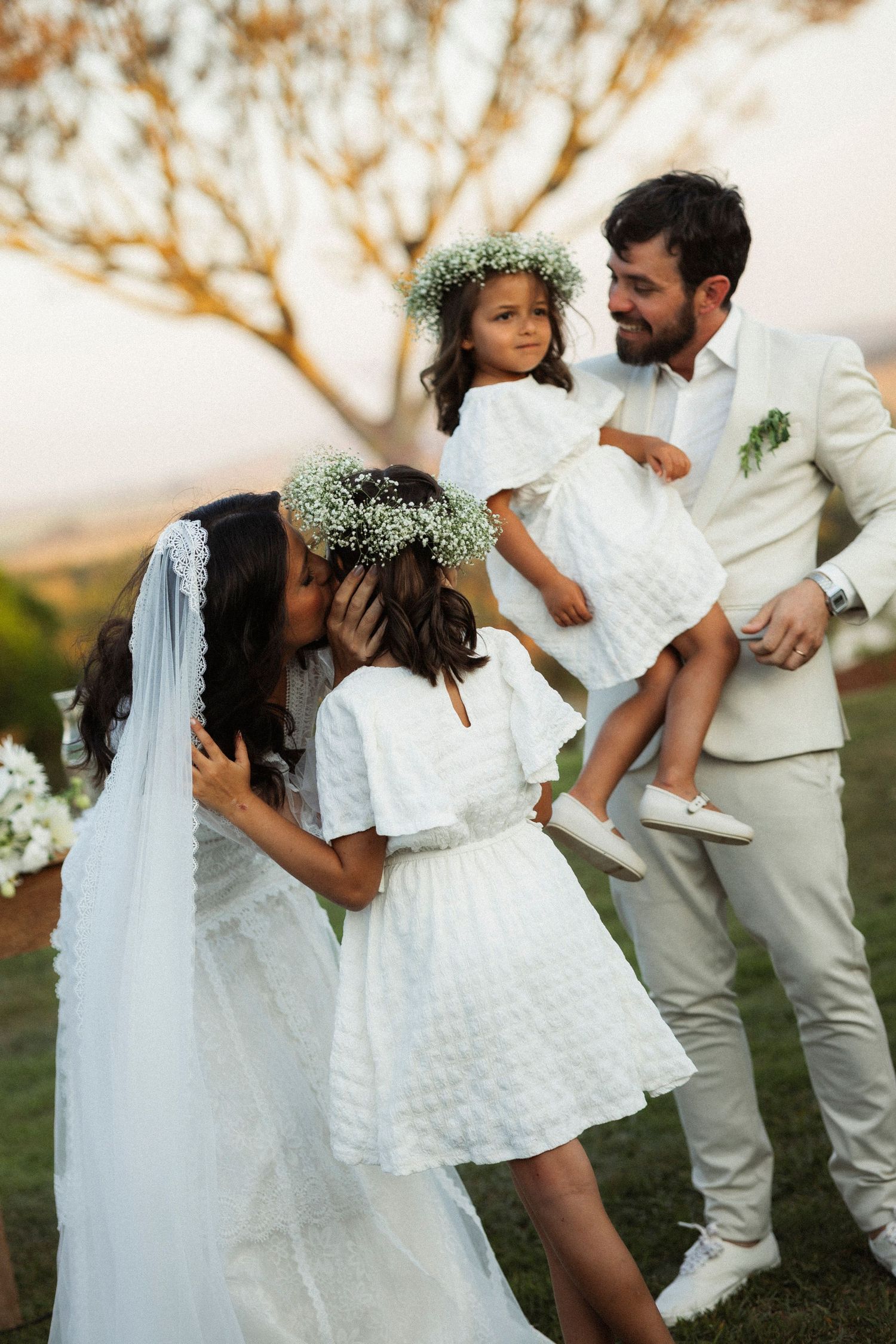 Wedding party in white and cream attire poses beneath flowering tree.
