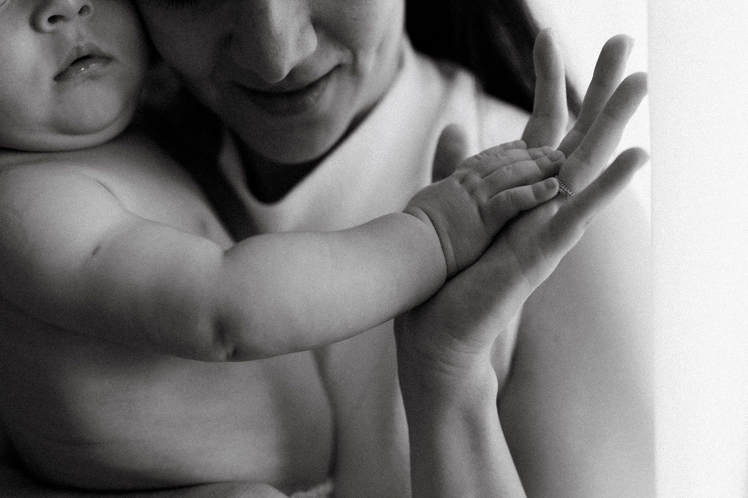 Black and white photo of a woman tenderly holding a baby, their hands intertwined in a loving embrace.