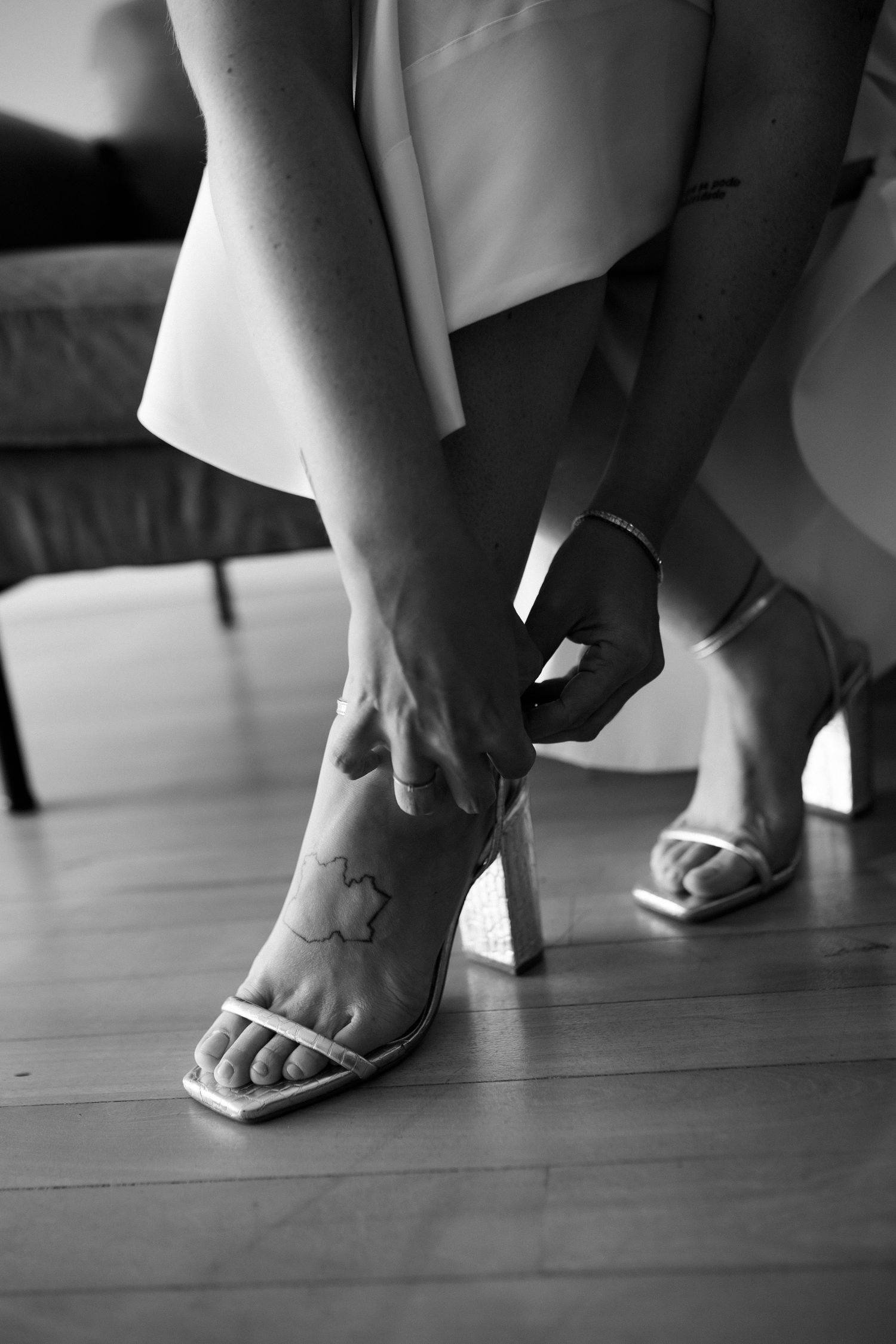 Close-up black and white photo of feet in wedding sandals with visible tattoo.