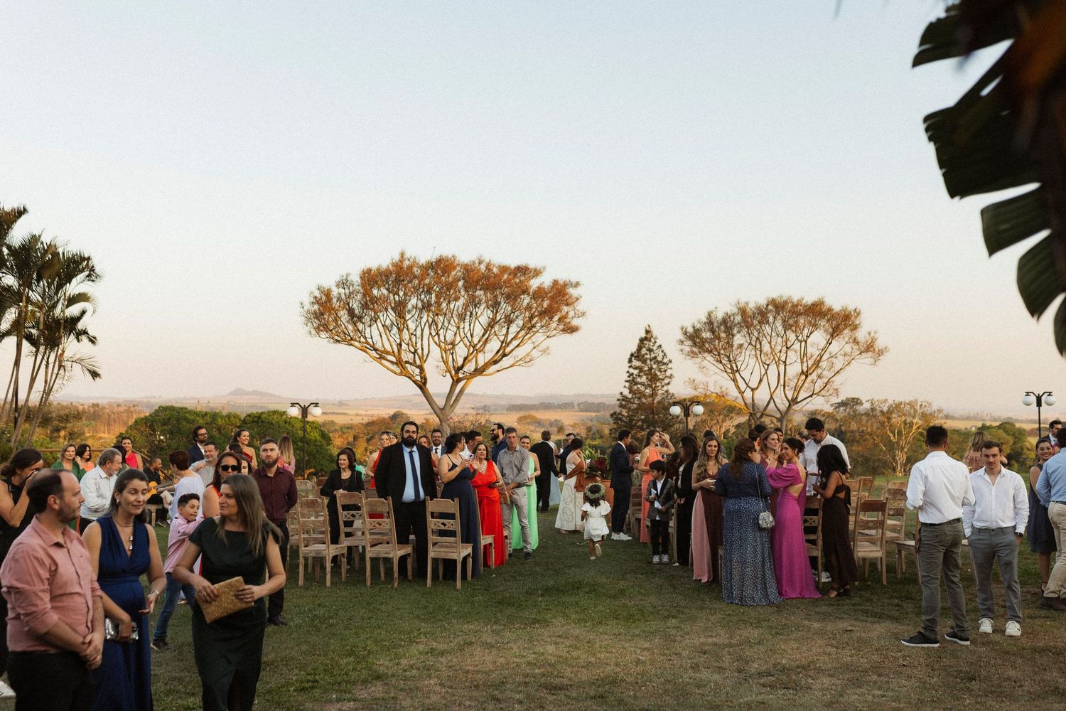 Wedding guests gather on lawn for outdoor celebration at sunset.