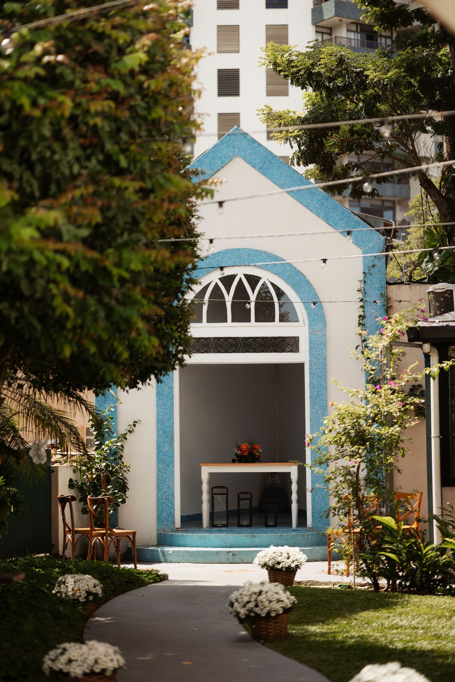 A white church building with blue trim and arched windows stands among green trees.