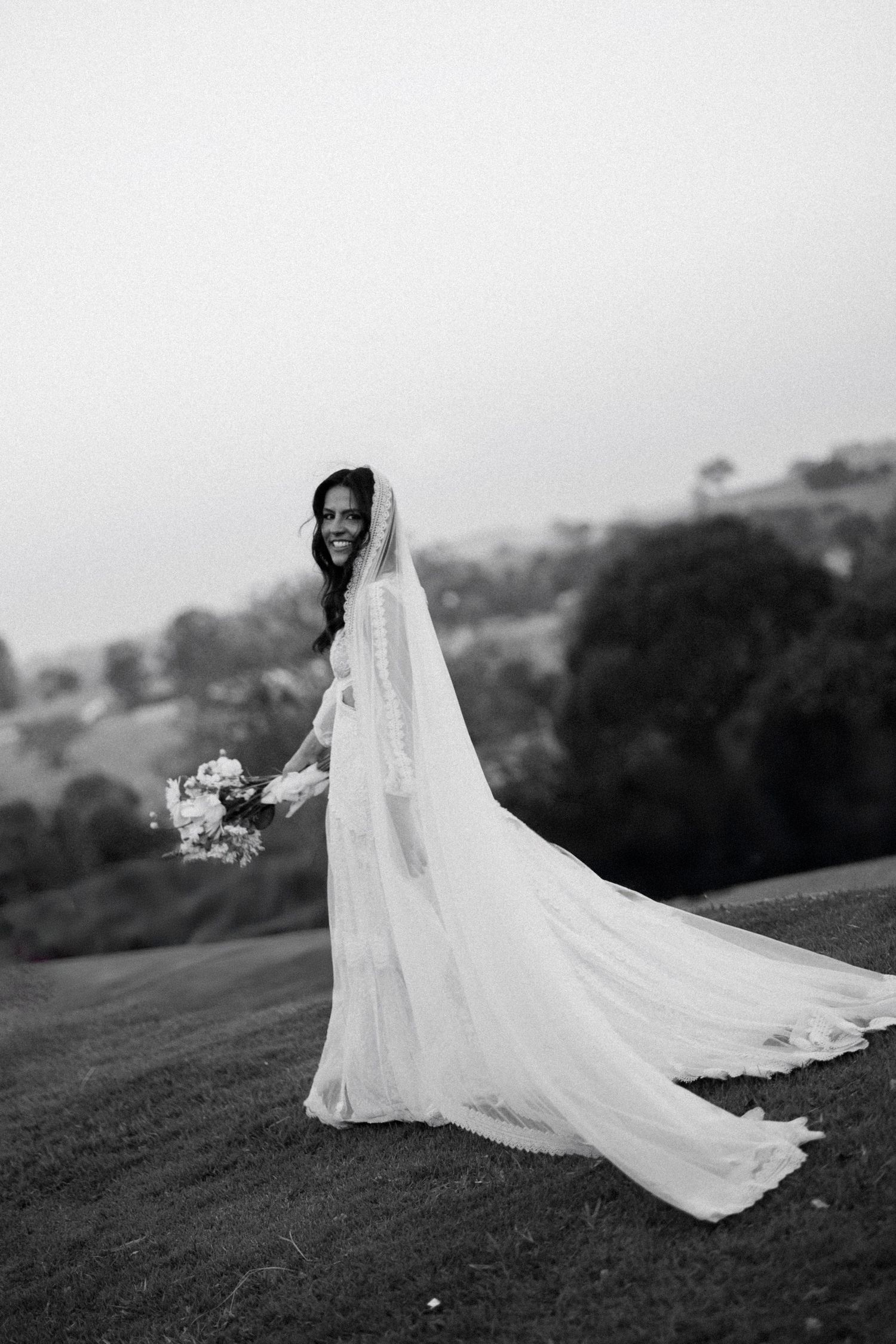 Dramatic black and white portrait of bride with flowing veil on rolling hillside.