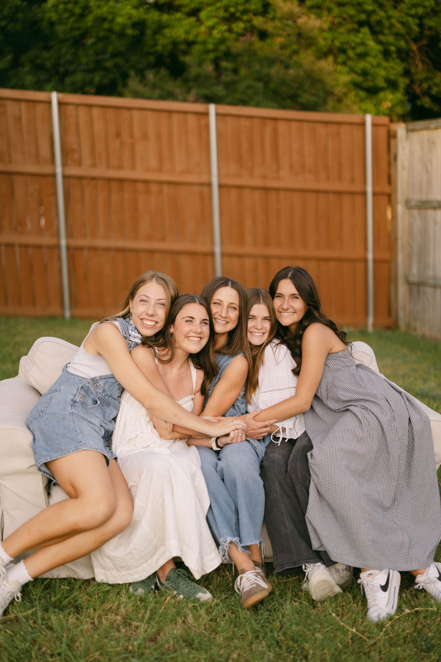 Friends lounging together on grass in casual outfits against a wooden fence.